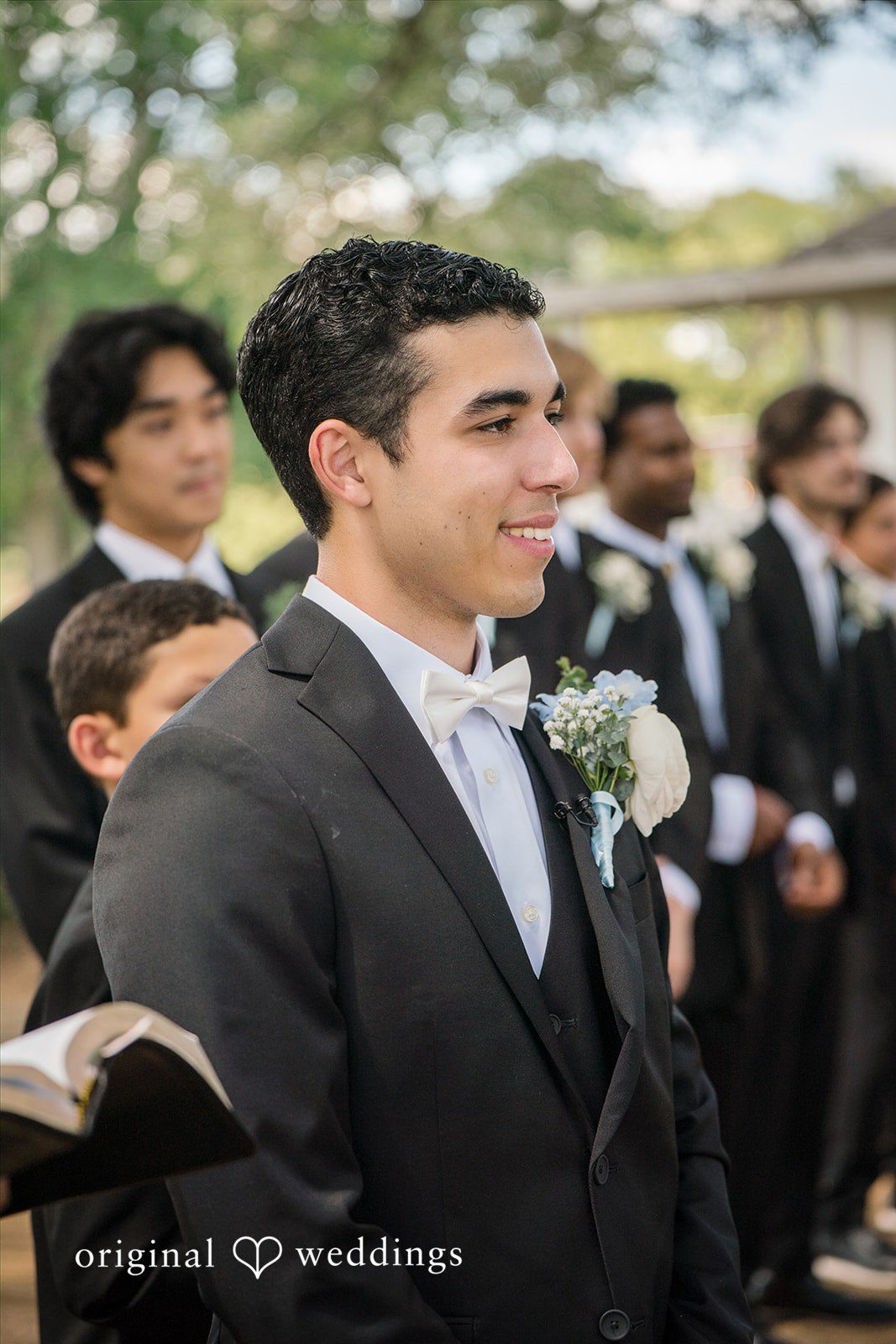 Morgan + Luke A groom smiles during the ceremony with groomsmen standing in the background.