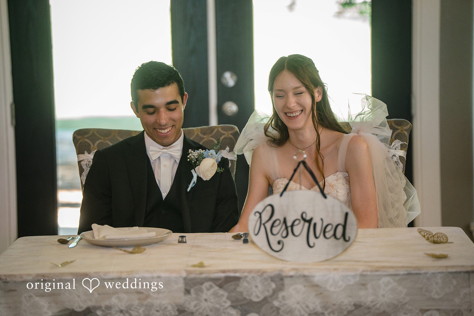 Morgan + Luke A seated bride and groom smile at a reception table .