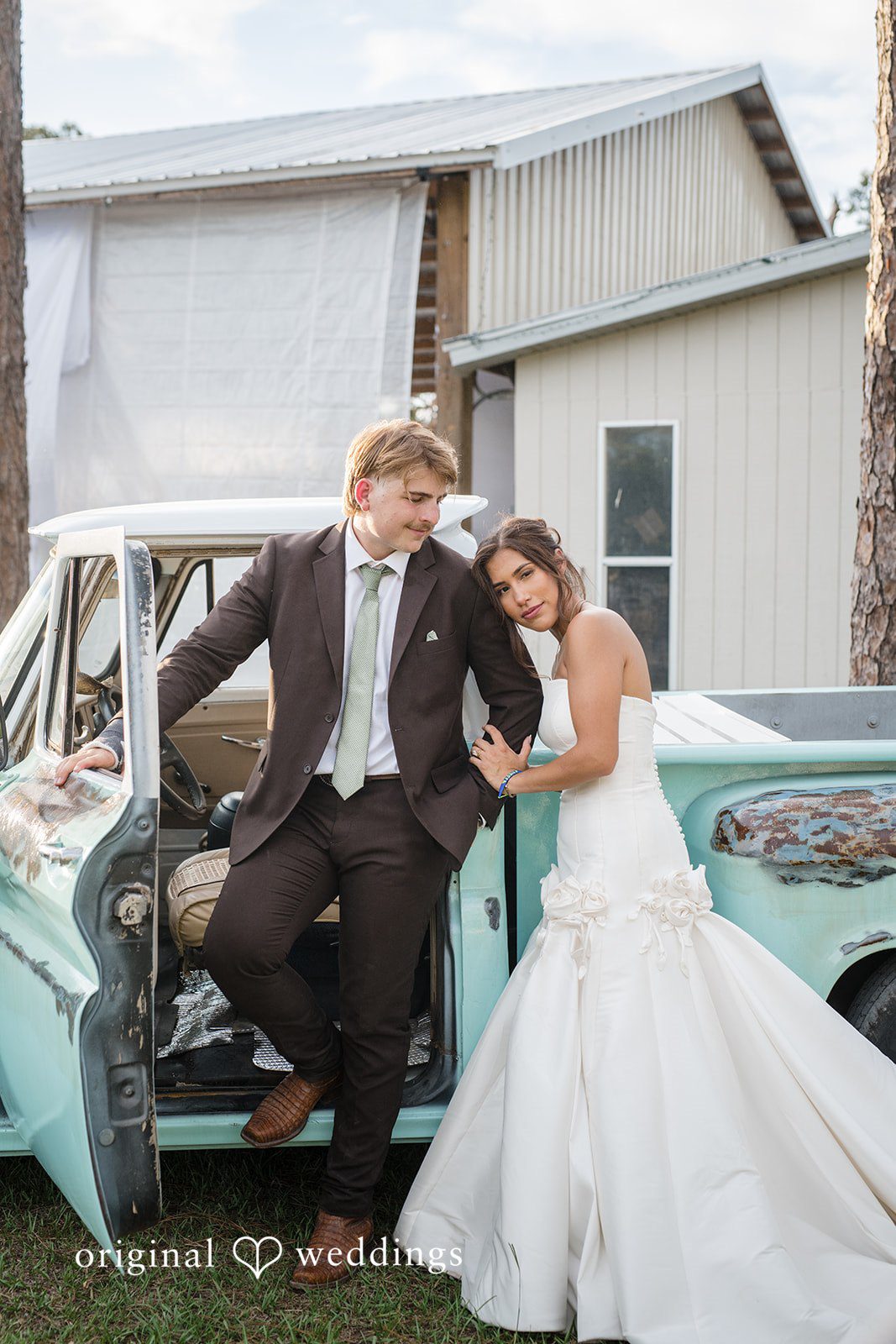 Bride standing on the car with her head resting on the groom's shoulder while the groom sits on the car at San Pedro Catholic Church
