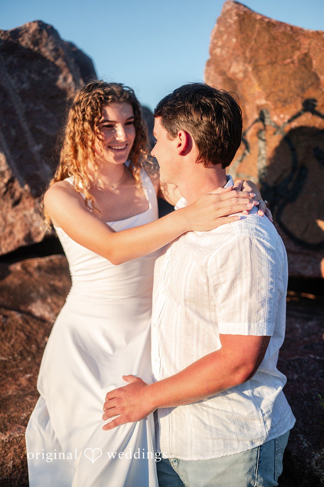 A man and a woman hugging in front of a large rocky background.