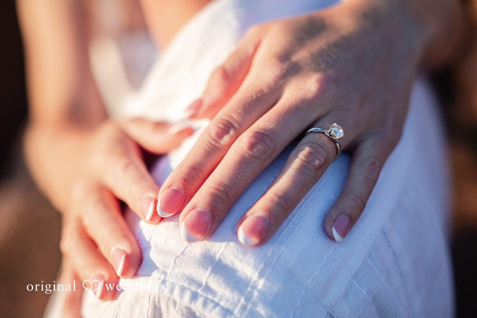 Close-up of a hand showing a ring resting on a white lace dress.