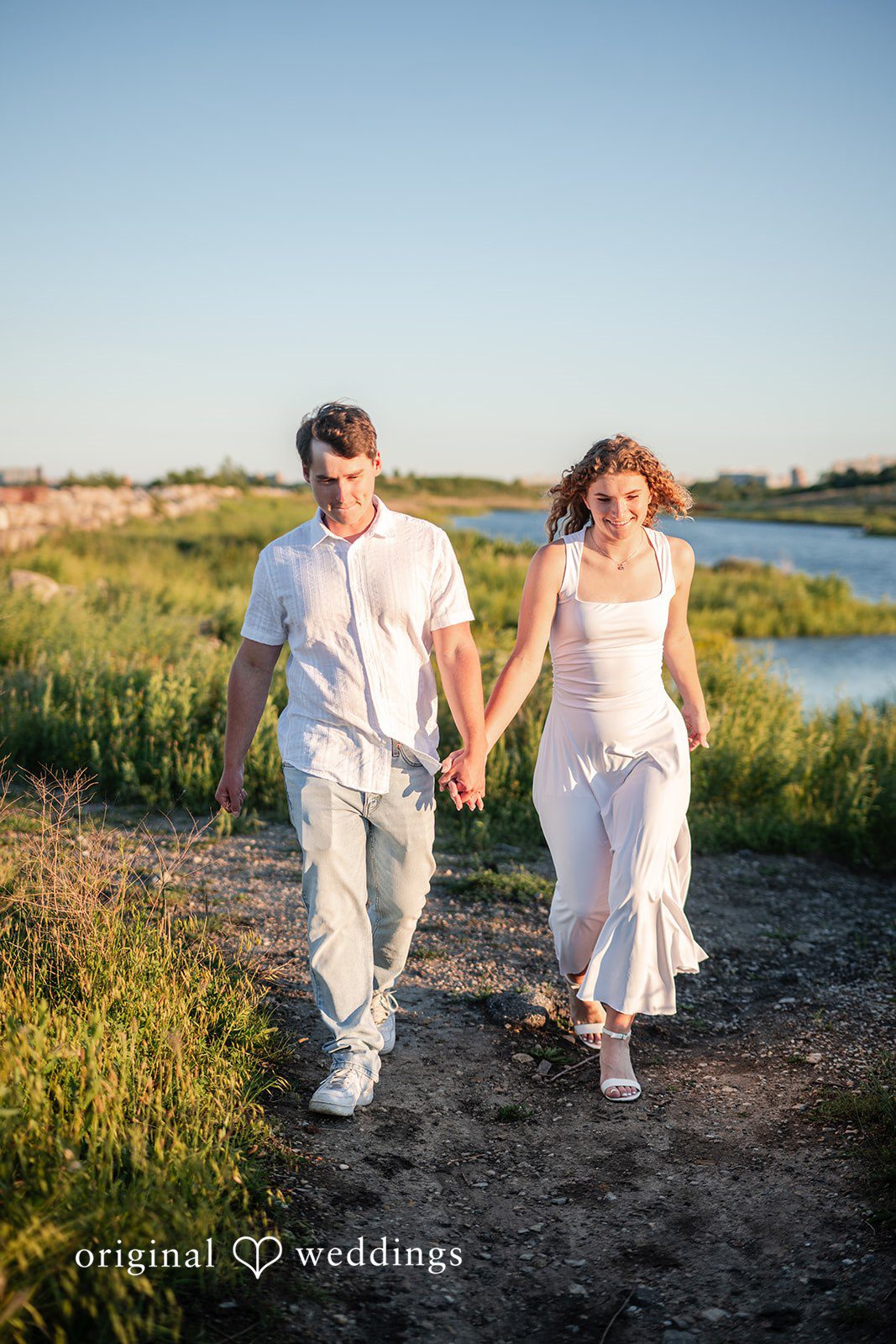 A Couple wearing white clothes running hand-in-hand through a field.