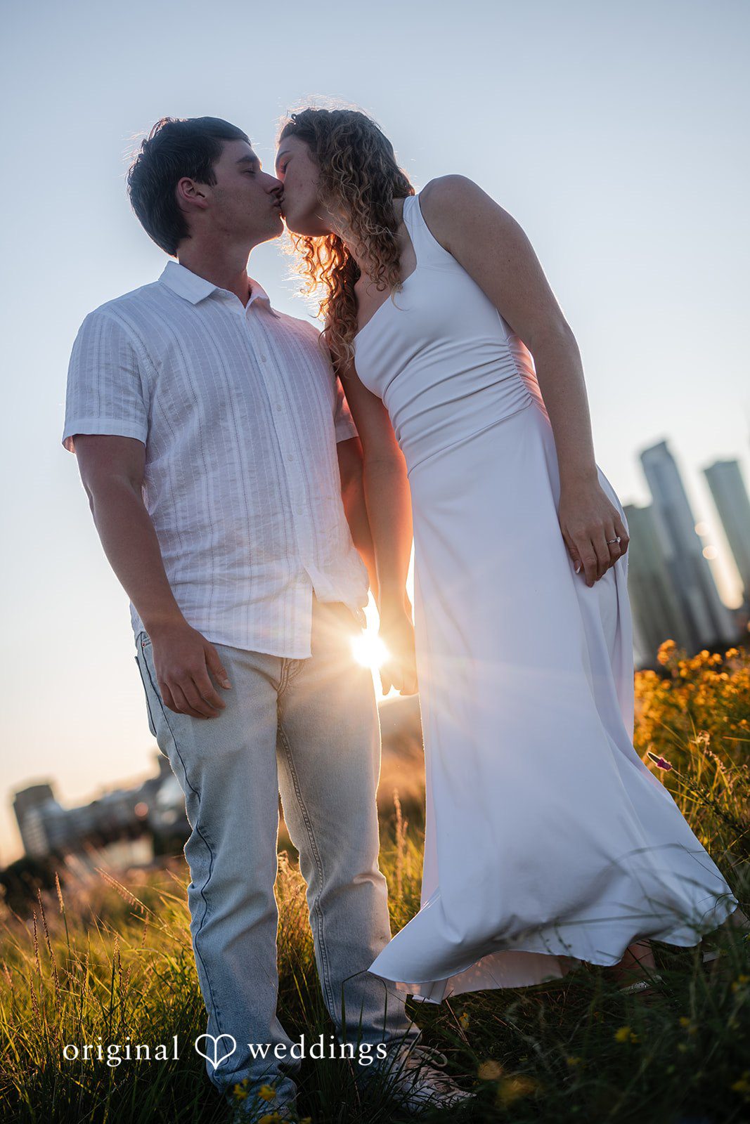 A Couple posing together with a city skyline in the background at sunset.