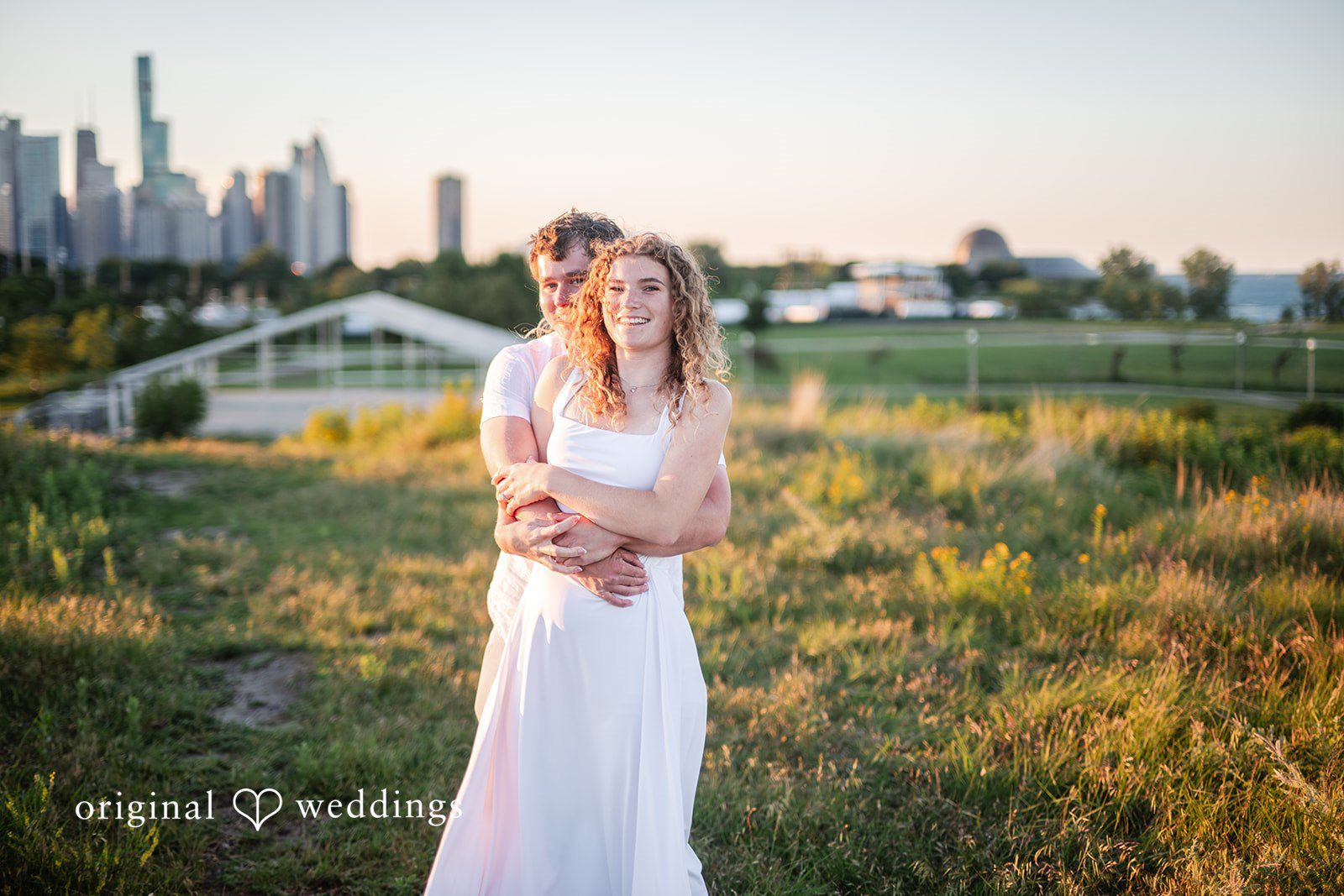 A couple in a white dress standing in a field of tall grass.