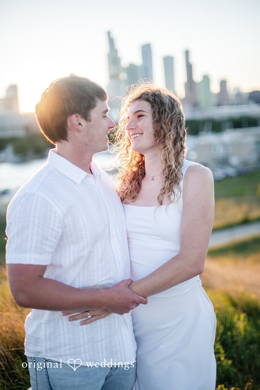 A couple looking lovingly at each other with a city skyline behind them.