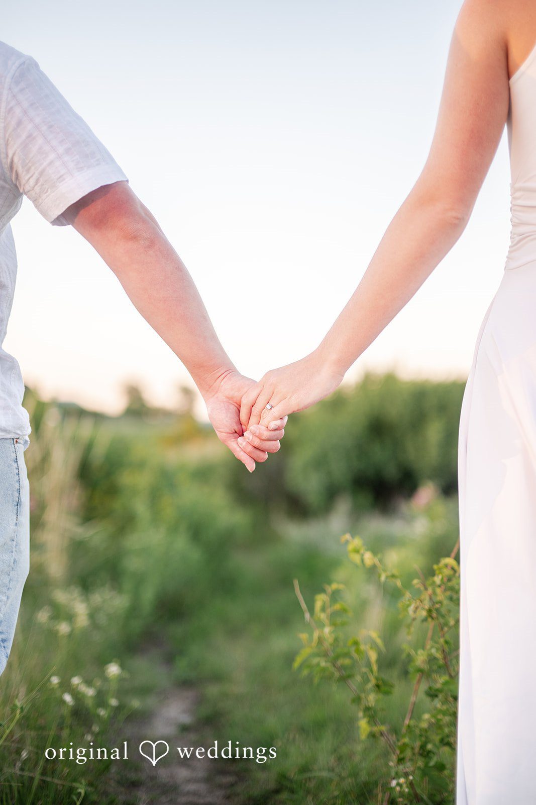 Two people holding hands while walking through a tall grassy field.