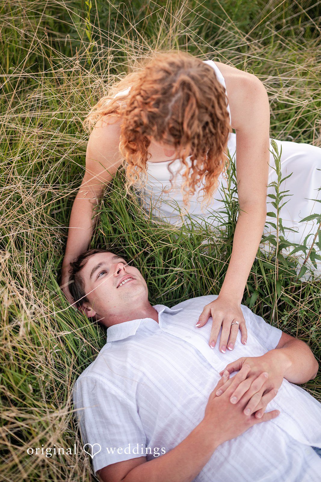 A woman leaning over a man who is lying down on his back in the grass.