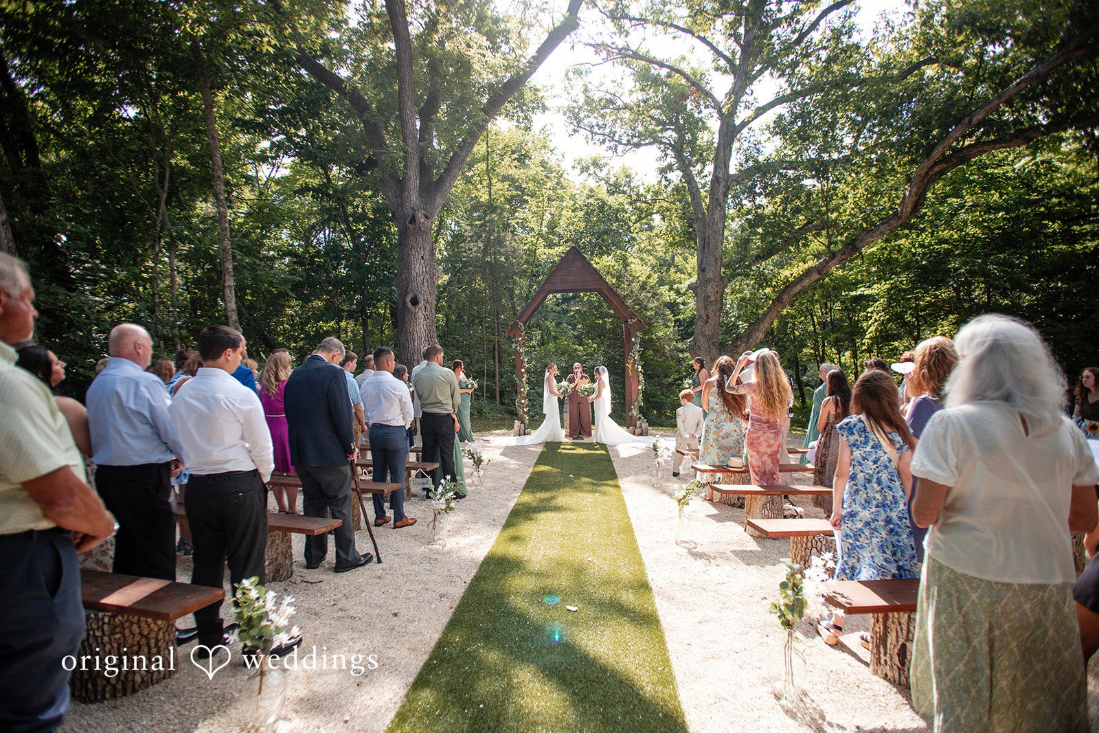Madison + Ally Rustic woodland wedding ceremony featuring two brides beneath a wooden arch