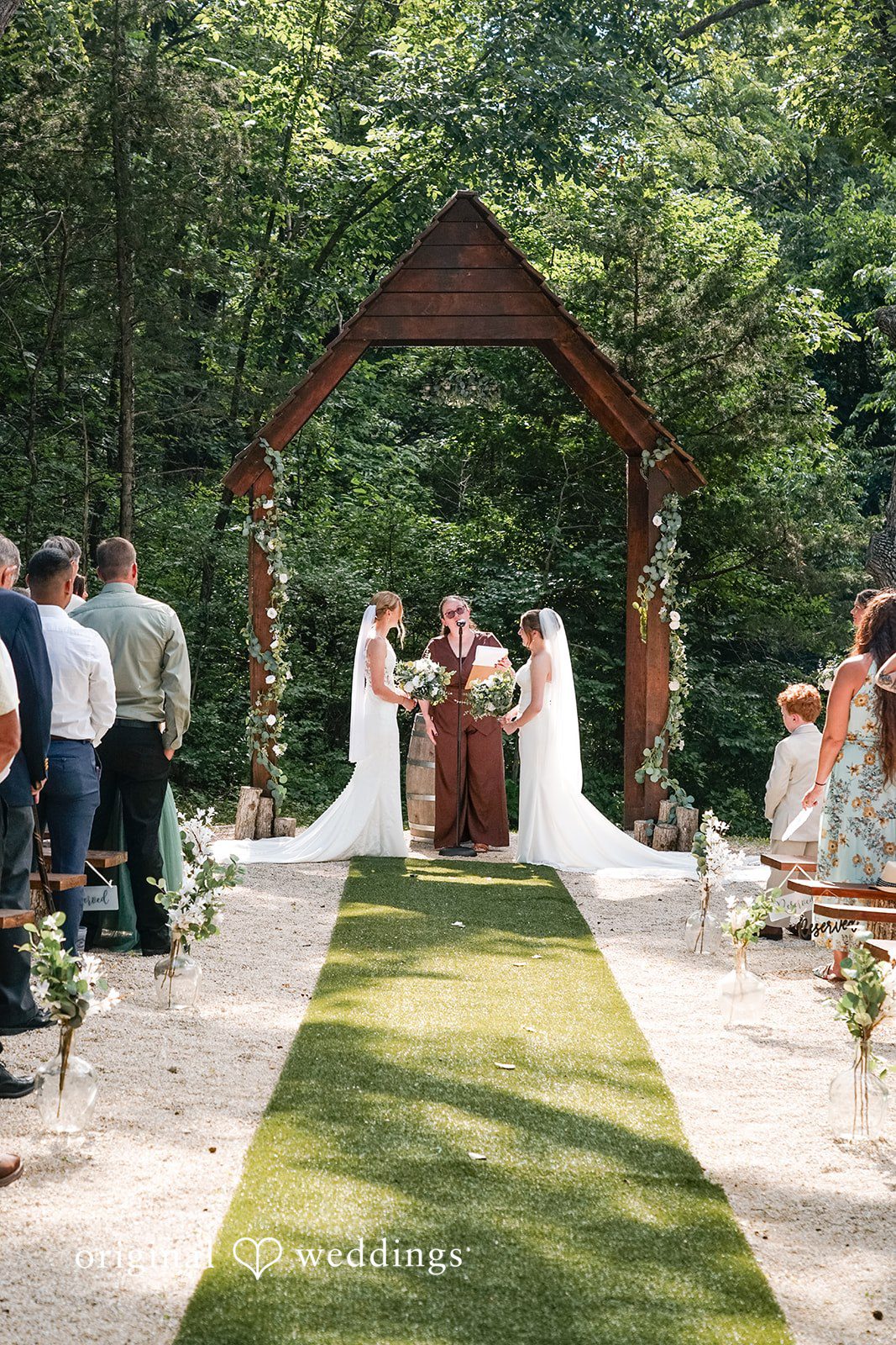 Madison + Ally Outdoor aisle leading to a beautiful ceremony surrounded by mature trees and wedding guests.