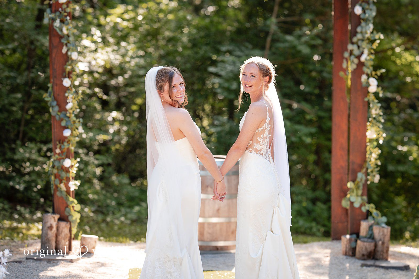 Madison + Ally Newlyweds looking back while holding hands beneath the rustic ceremony arbor.