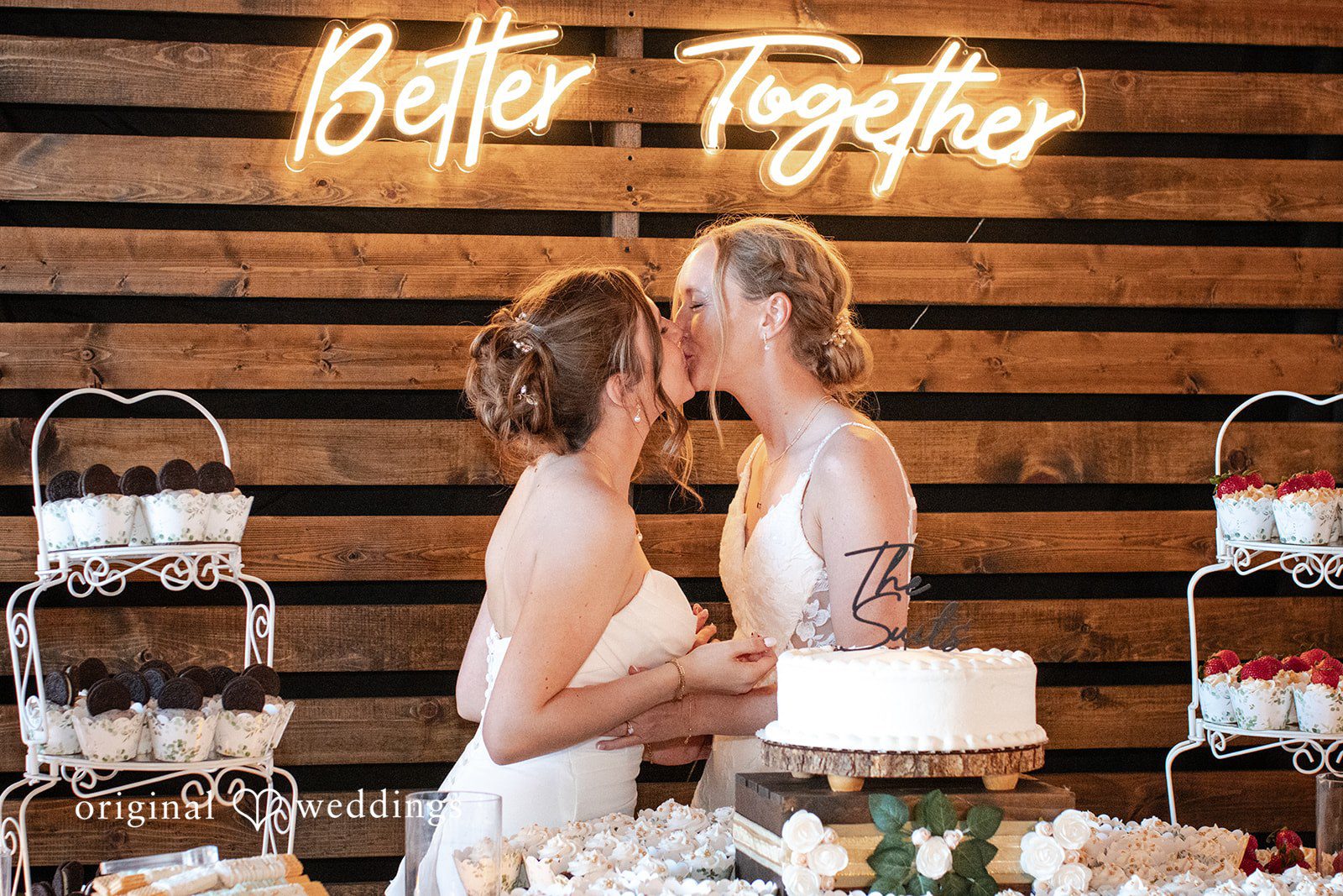 Madison + Ally Brides sharing a kiss beside their wedding cake at The Barn at Matson Hill