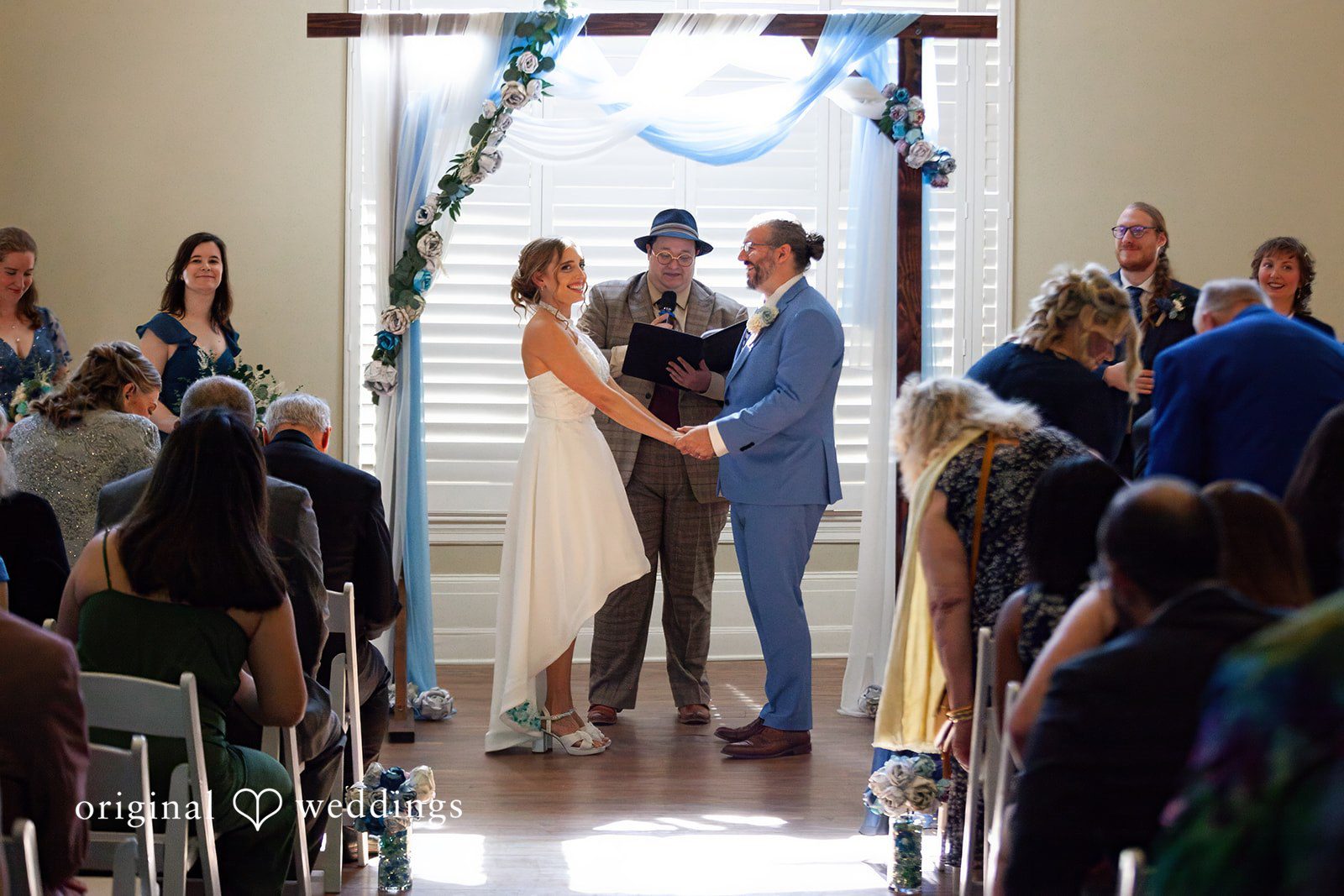Sasha + Tom Bride and groom holding hands before the priest during ceremony at The Great Hall at Green Lake