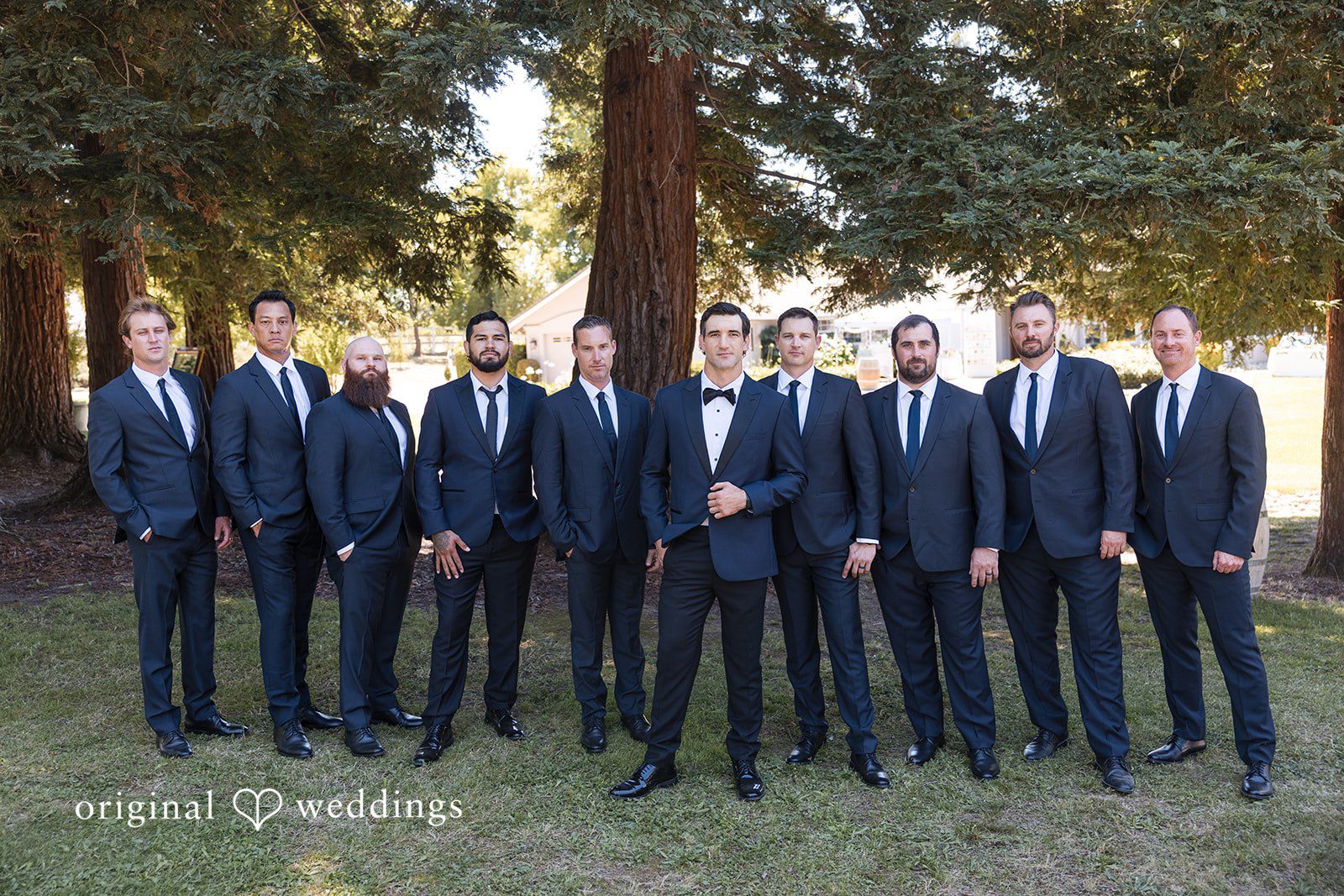 Avery + Ryan Groom and groomsmen in matching dark suits posing together under the trees.