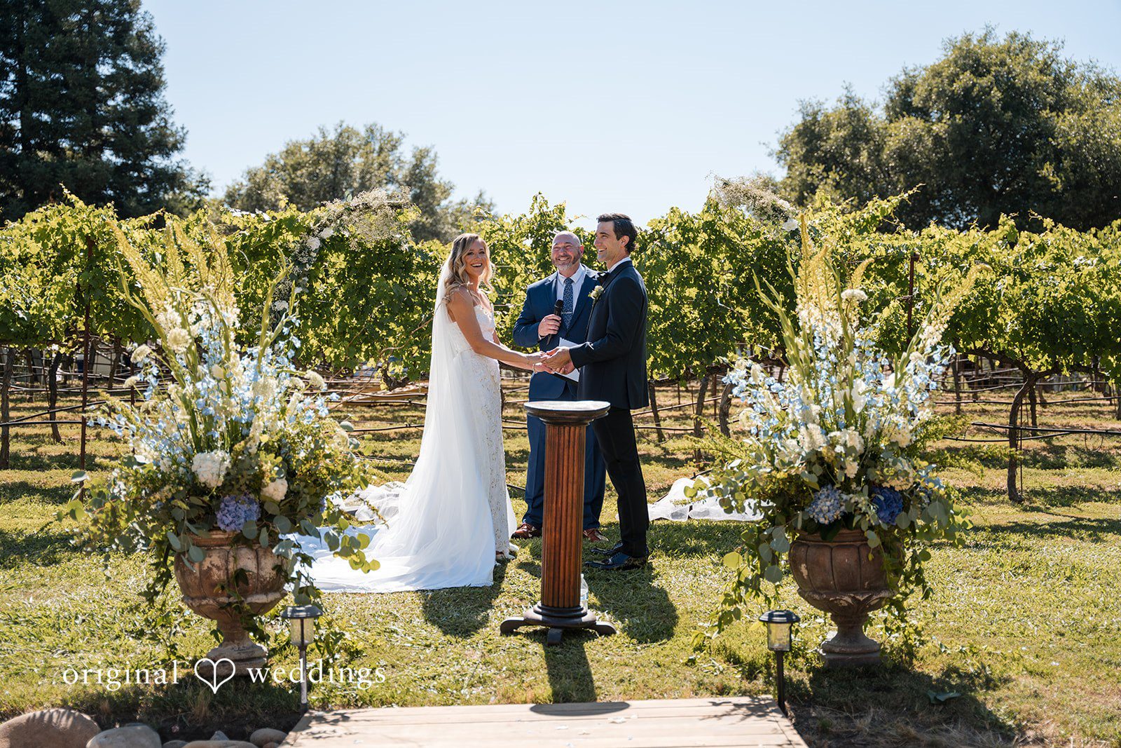 Avery + Ryan A bride and groom standing at the altar during an open-air ceremony by a vineyard.