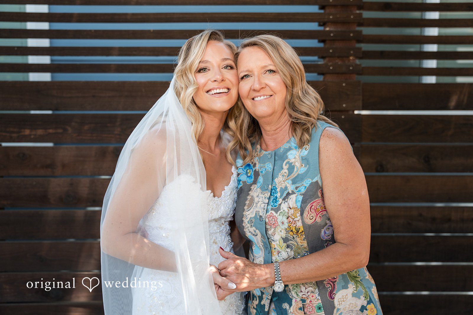 Avery + Ryan A bride wearing a veil posing affectionately with a woman in a floral dress.