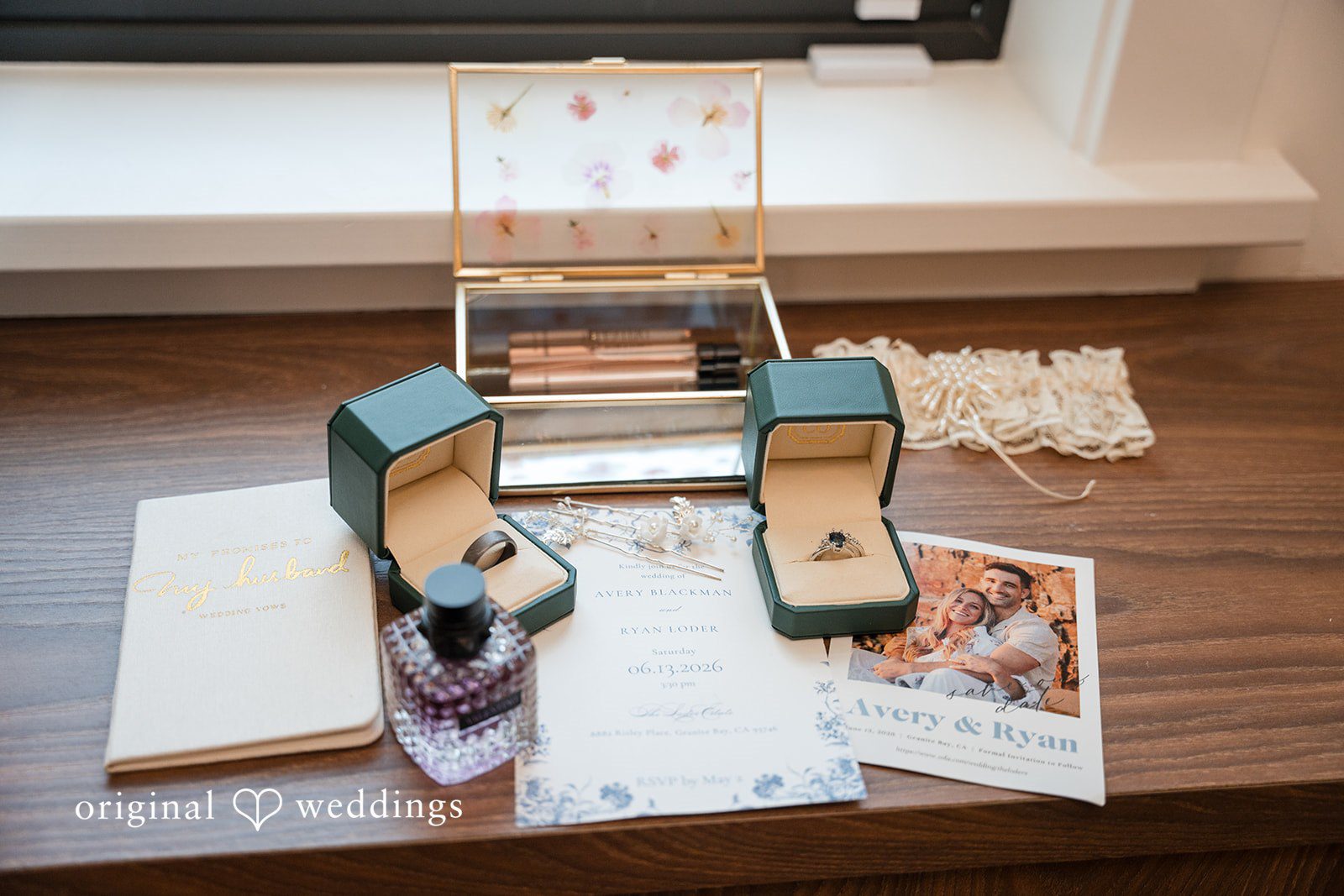 Avery + Ryan Wedding rings presented in open velvet jewelry boxes alongside custom stationery on a table.