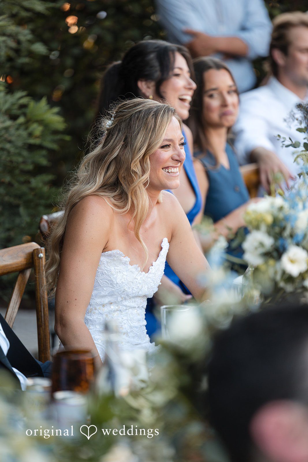 Avery + Ryan A smiling bride sitting at a reception table surrounded by laughing guests.