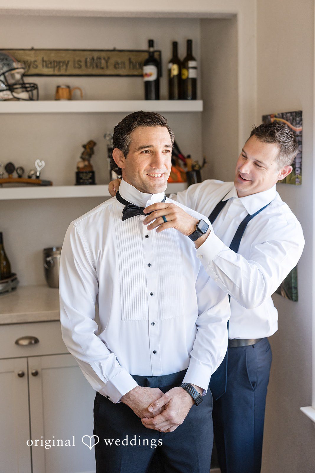 Avery + Ryan A groomsman helping a groom adjust his bow tie while getting ready.