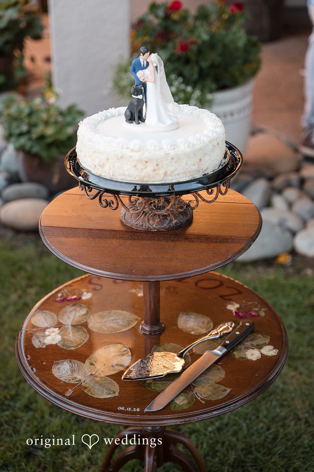 Avery + Ryan A multi-tiered rustic wooden stand holding a white wedding cake and decorative items.