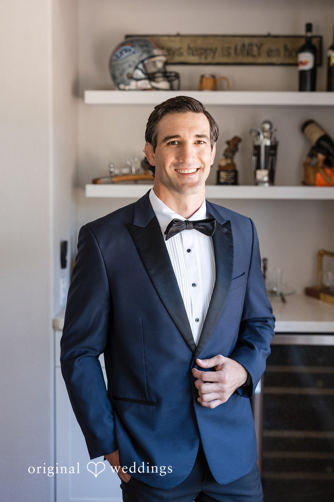 Avery + Ryan A smiling groom posing solo in a sharp navy blue tuxedo with black lapels.