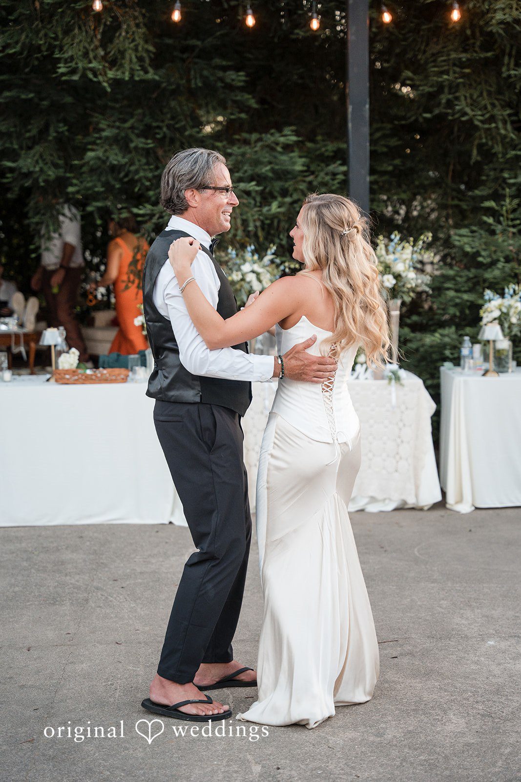 Avery + Ryan A bride smiling warmly while dancing with a man wearing a vest and glasses.