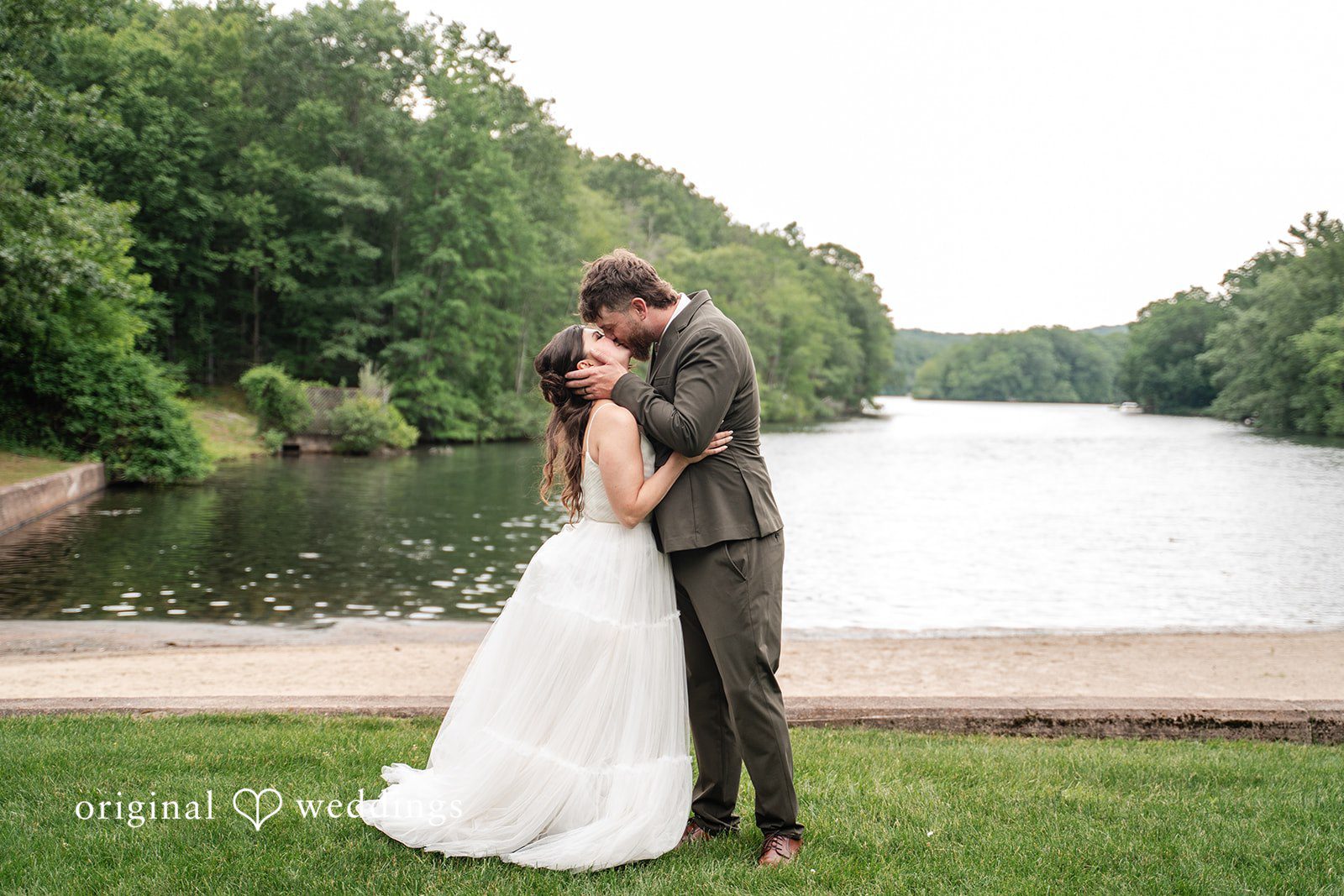 Elegant newlywed picture featuring a romantic kiss with beautiful waterfront views.