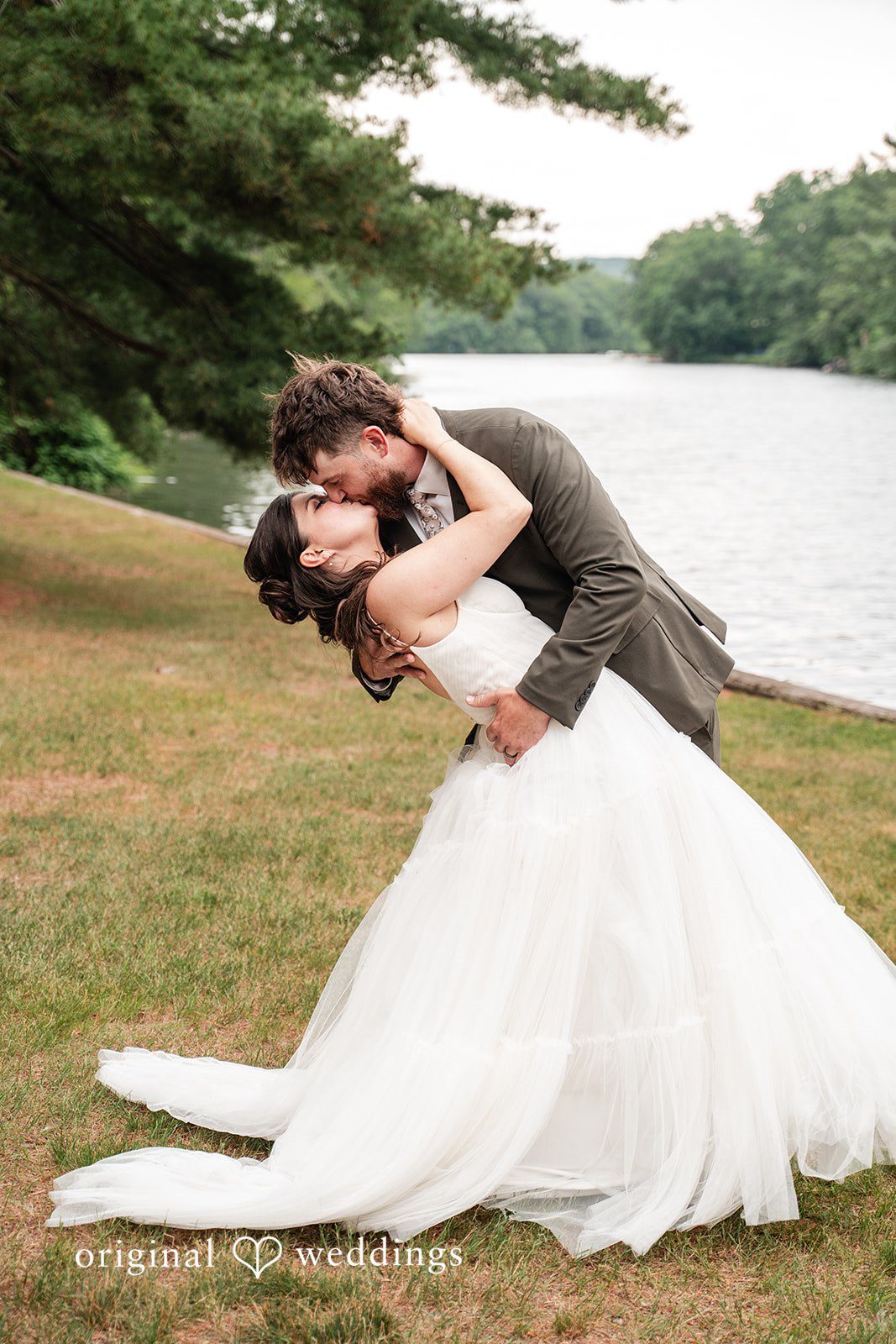 Elegant newlywed portrait featuring a romantic kiss with beautiful waterfront views