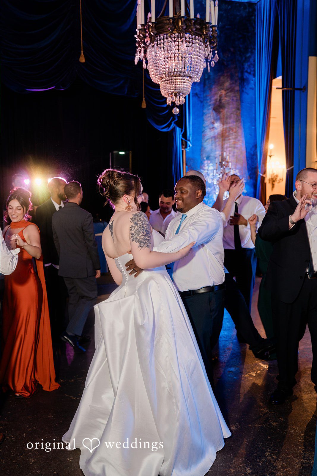Madison + Malik A couple dancing dynamically under dramatic blue event lighting and a chandelier.