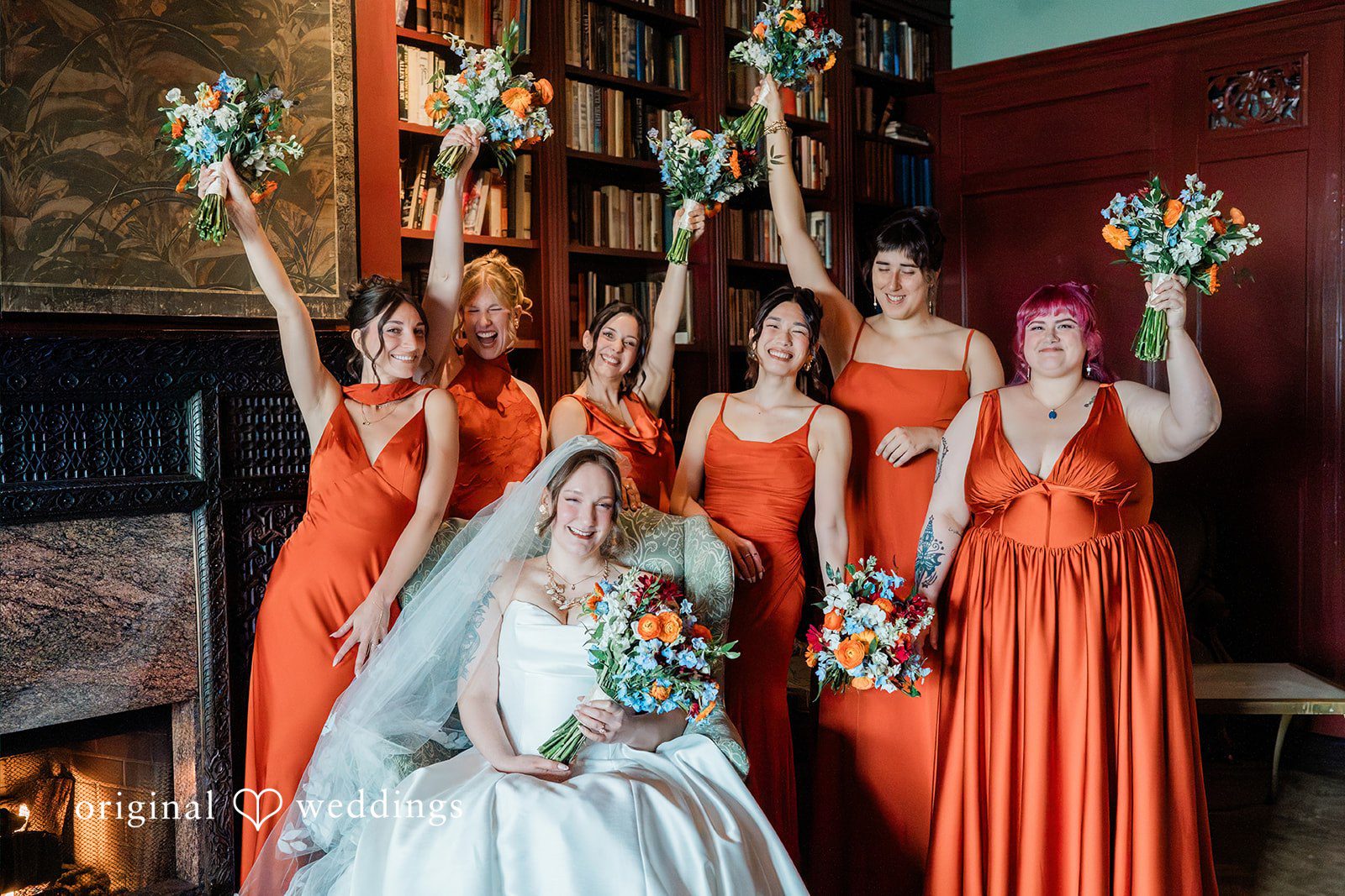 Madison + Malik A bride posing with bridesmaids dressed in vibrant orange gowns.