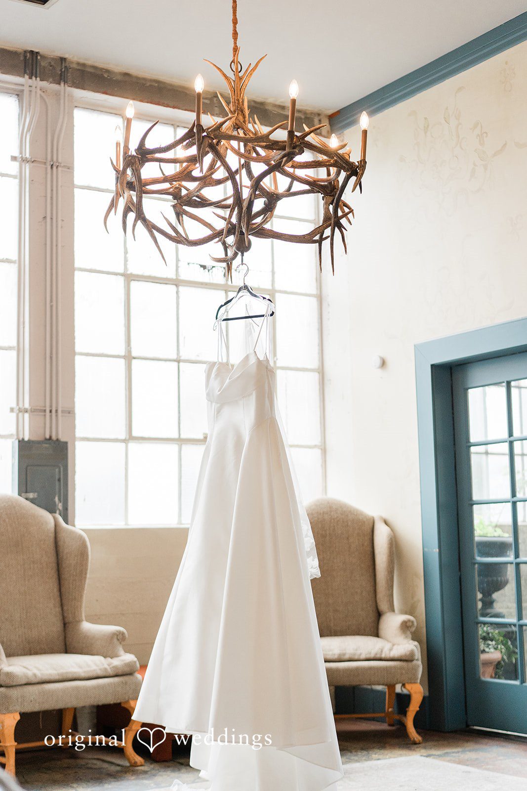 Madison + Malik A white wedding gown hanging from a rustic wooden chandelier.