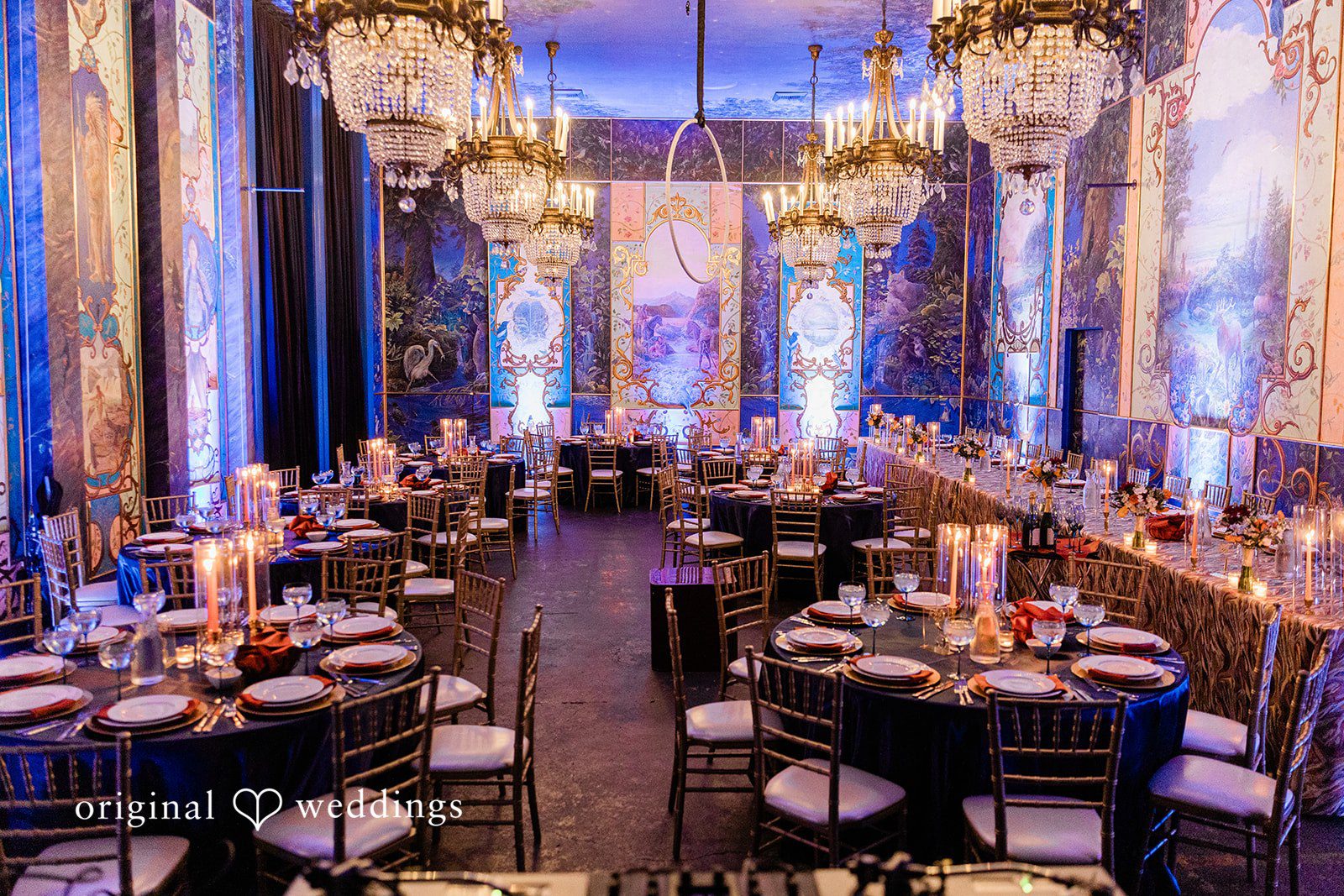 Madison + Malik A reception hall featuring round tables with dark blue linens and dramatic purple lighting.