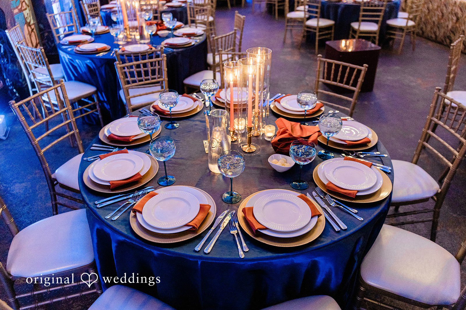 Madison + Malik A close-up of a circular dinner table set with gold-rimmed plates and navy blue tablecloths.