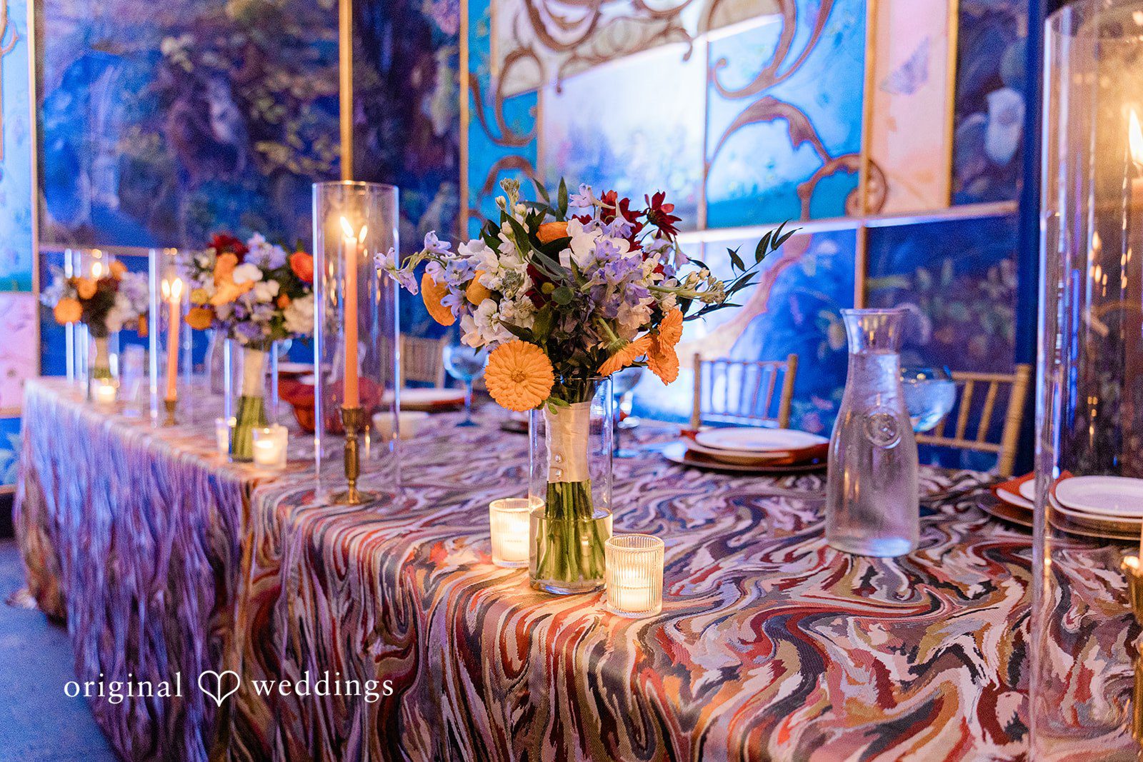 Madison + Malik A long head table decorated with tall floral arrangements and candles.