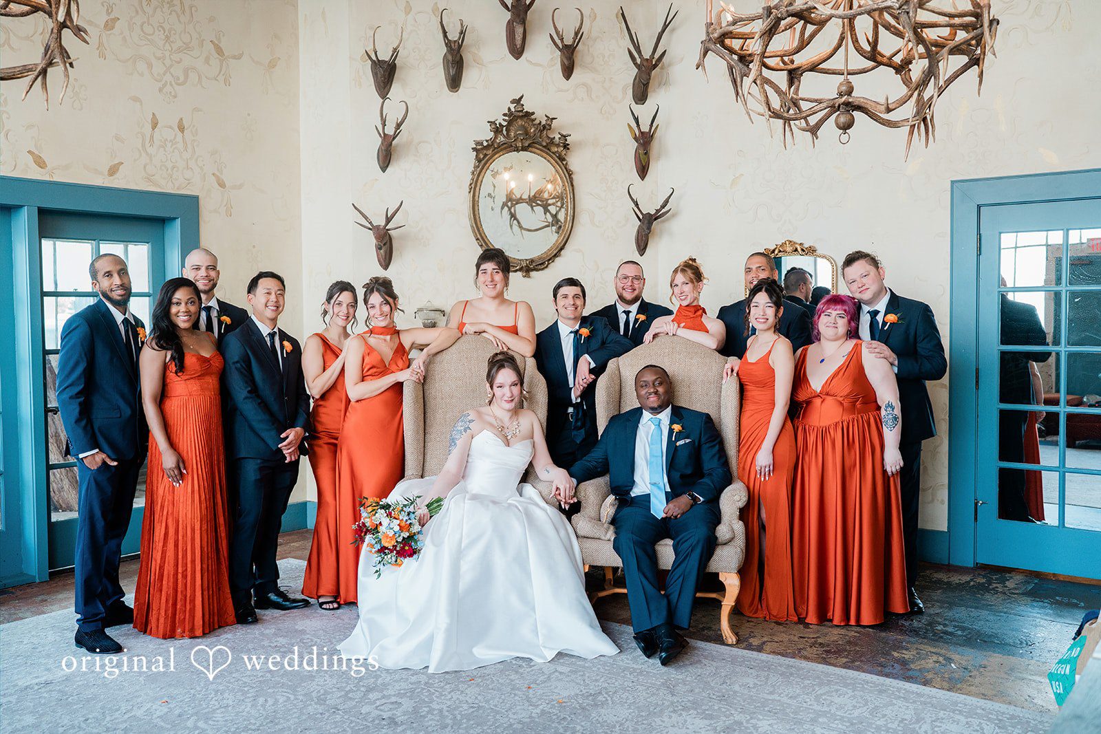 Madison + Malik A large wedding party with bridesmaids in orange gowns posing together.