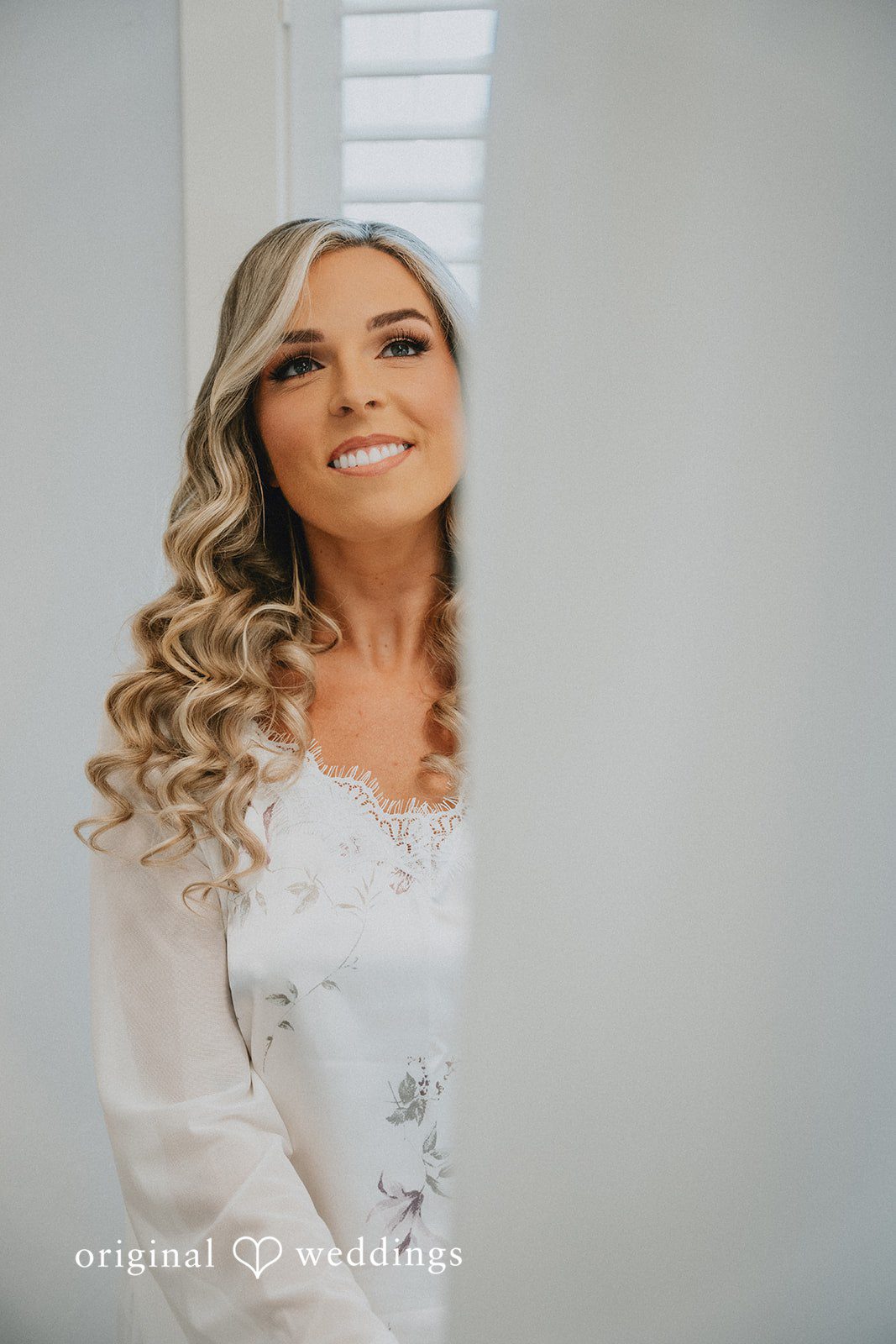 Kaylee + Raul A blonde bride peeking out from behind a white wall while smiling.