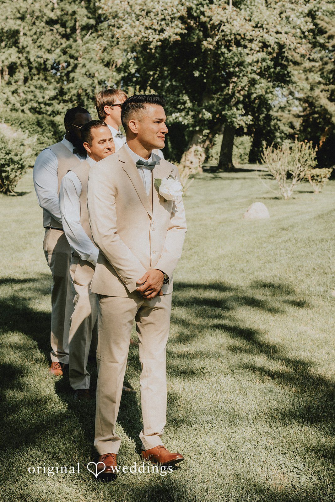 Kaylee + Raul A groom standing on a grassy field surrounded by groomsmen in tan suits.