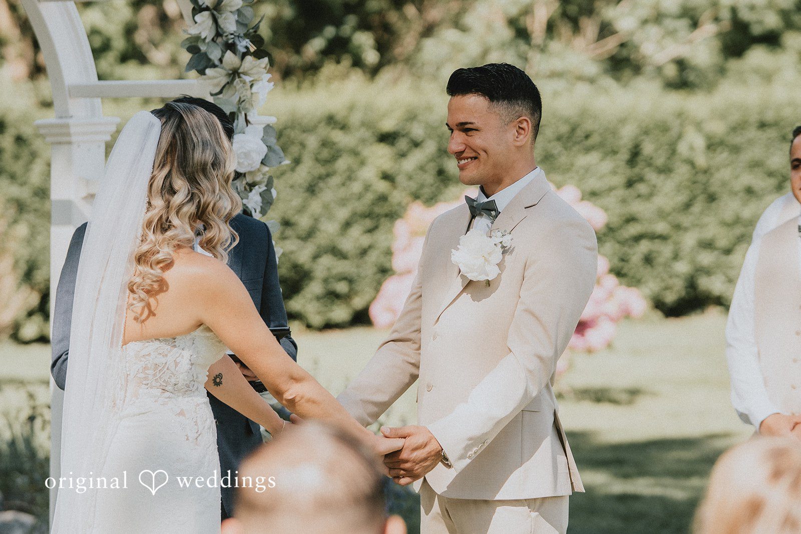 Kaylee + Raul A groom smiling while holding hands with his bride during their wedding ceremony.