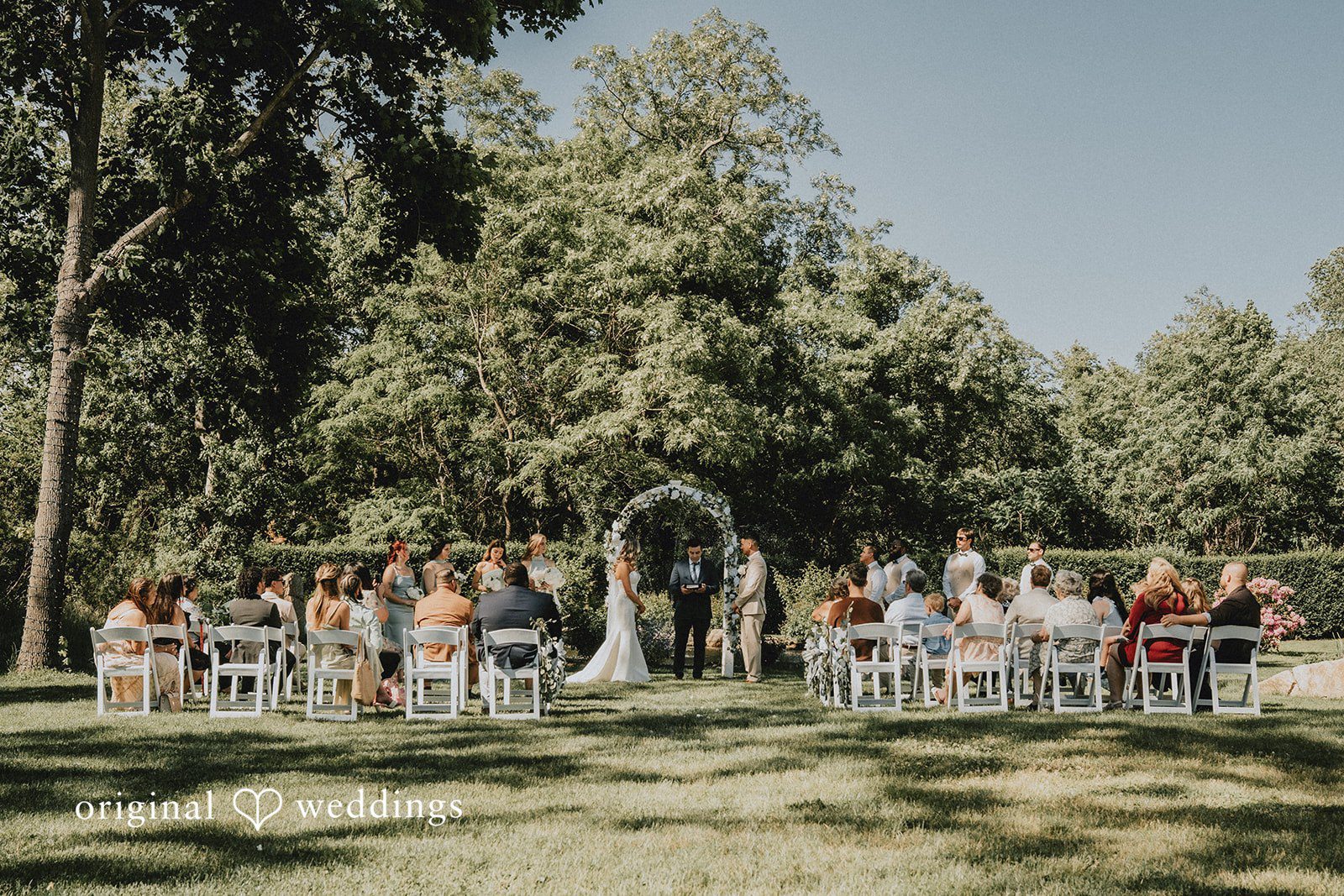 Kaylee + Raul distant view of a wedding ceremony with guests seated in rows on a lawn.