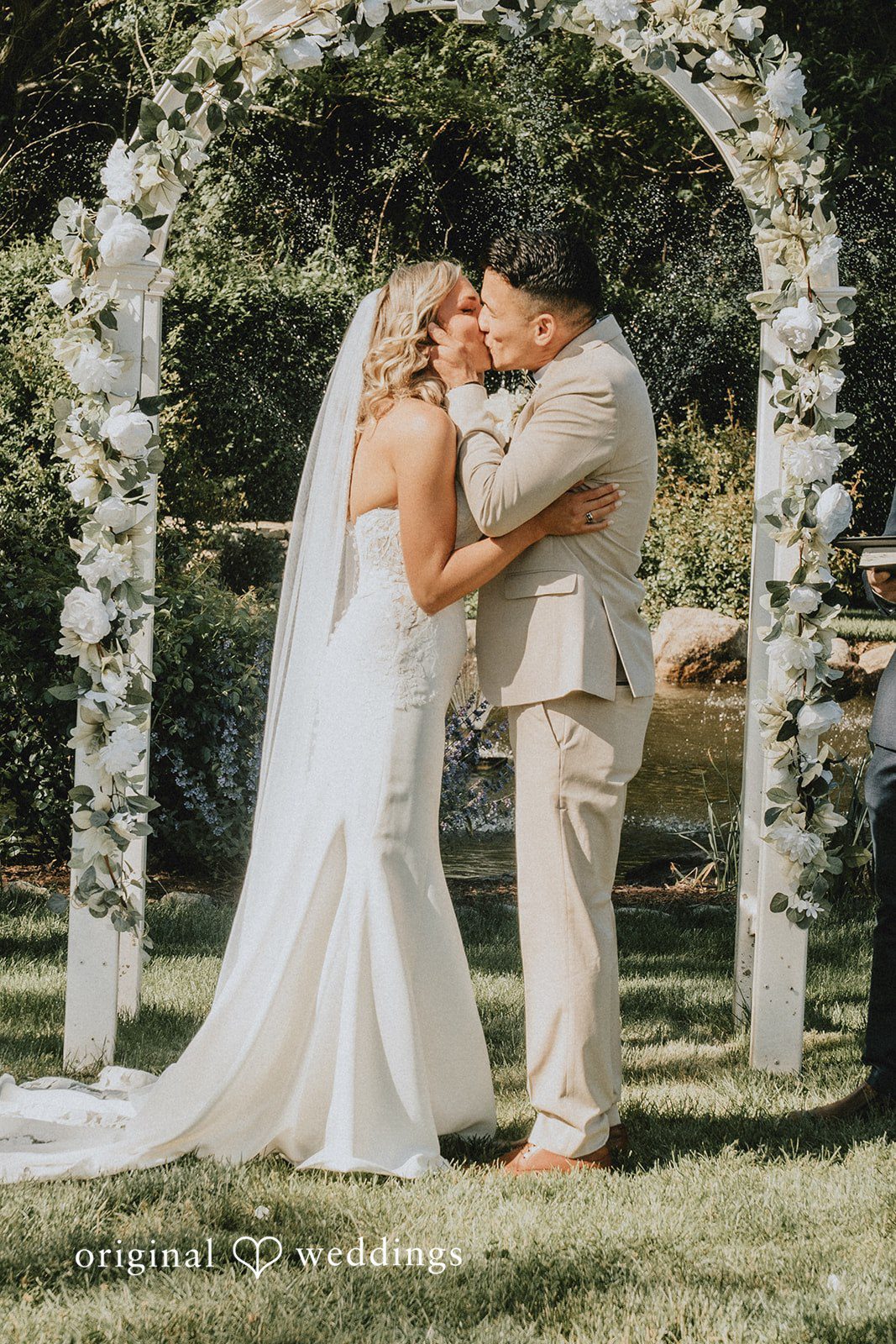 Kaylee + Raul A bride and groom sharing a kiss under a stone wedding archway.