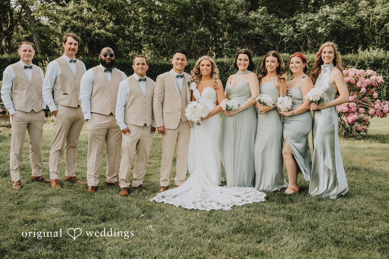 Kaylee + Raul The full wedding party posing together on a grassy lawn lined with trees.