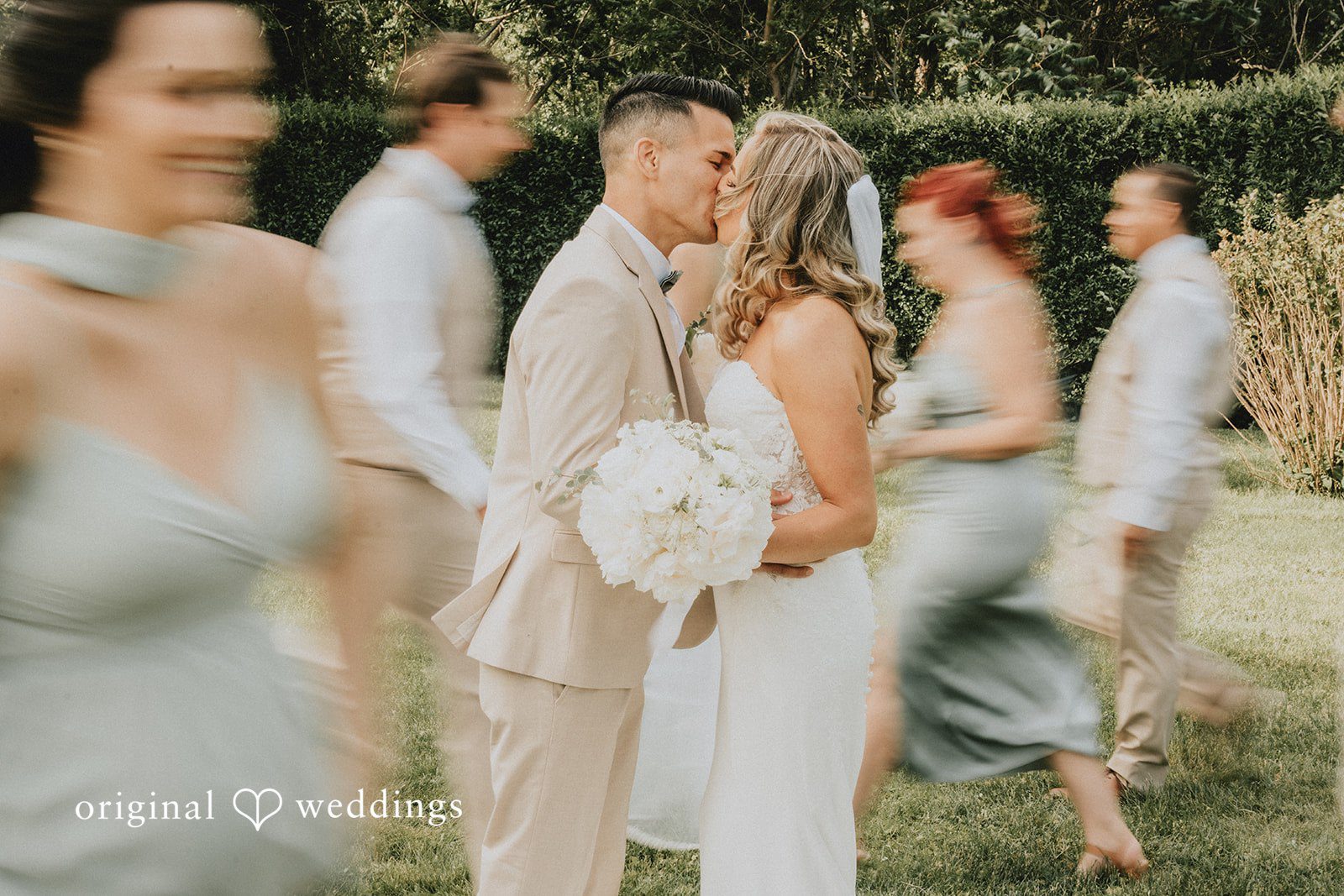 Kaylee + Raul A bride and groom kissing while surrounded by their bridesmaids and groomsmen.