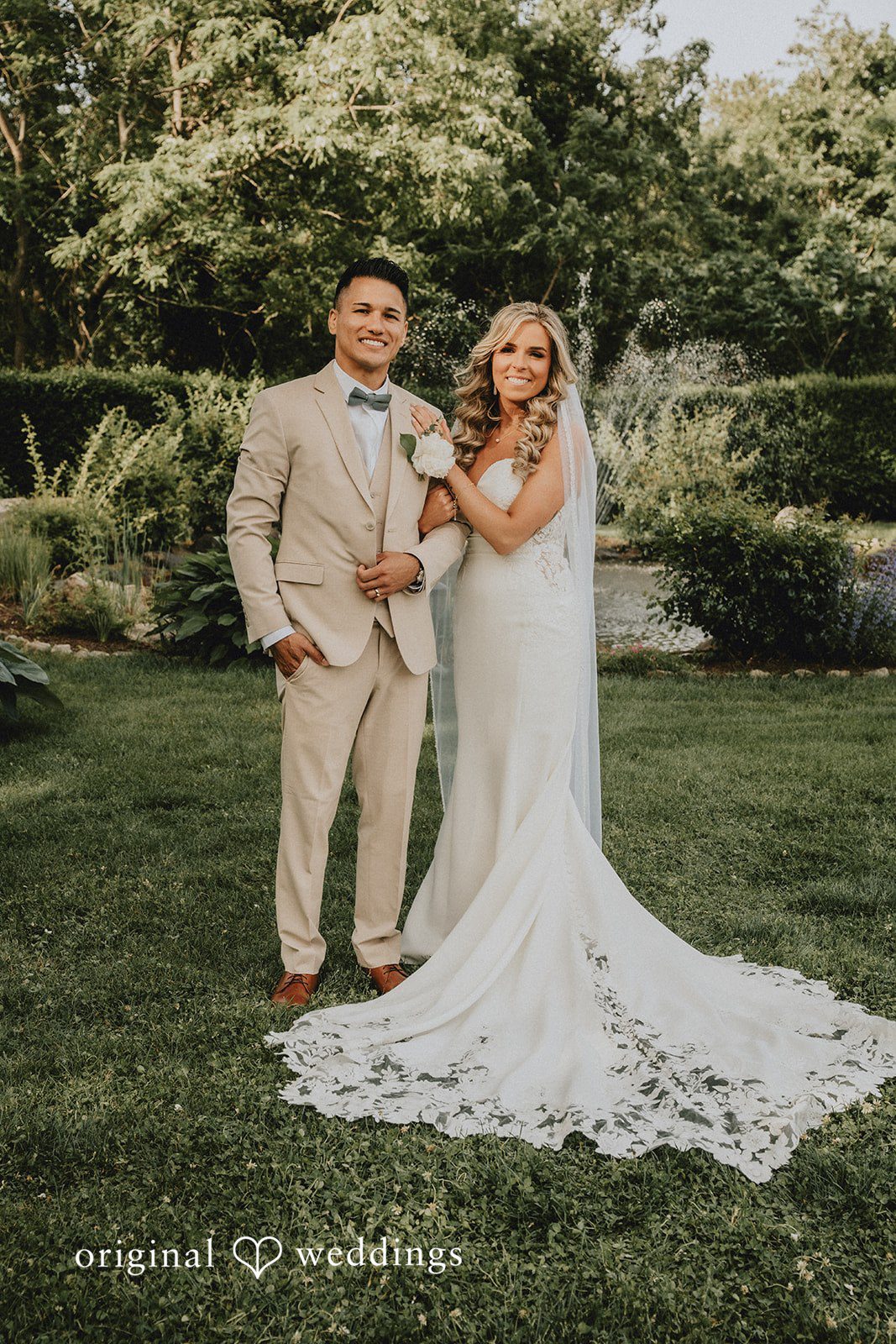 Kaylee + Raul A bride and groom posing together on a grassy field in front of green trees.