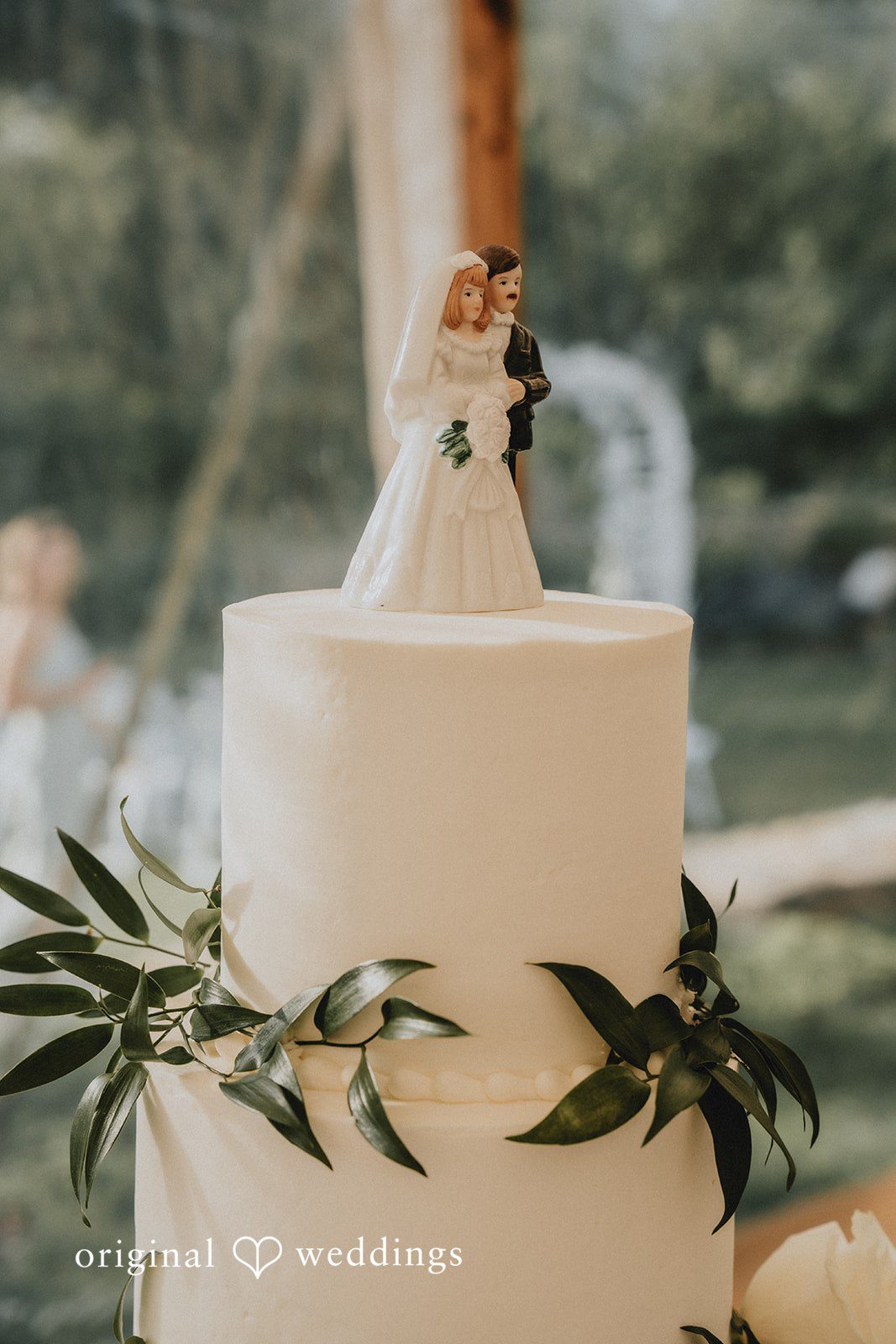 Kaylee + Raul A close-up shot of a white wedding cake decorated with green foliage.