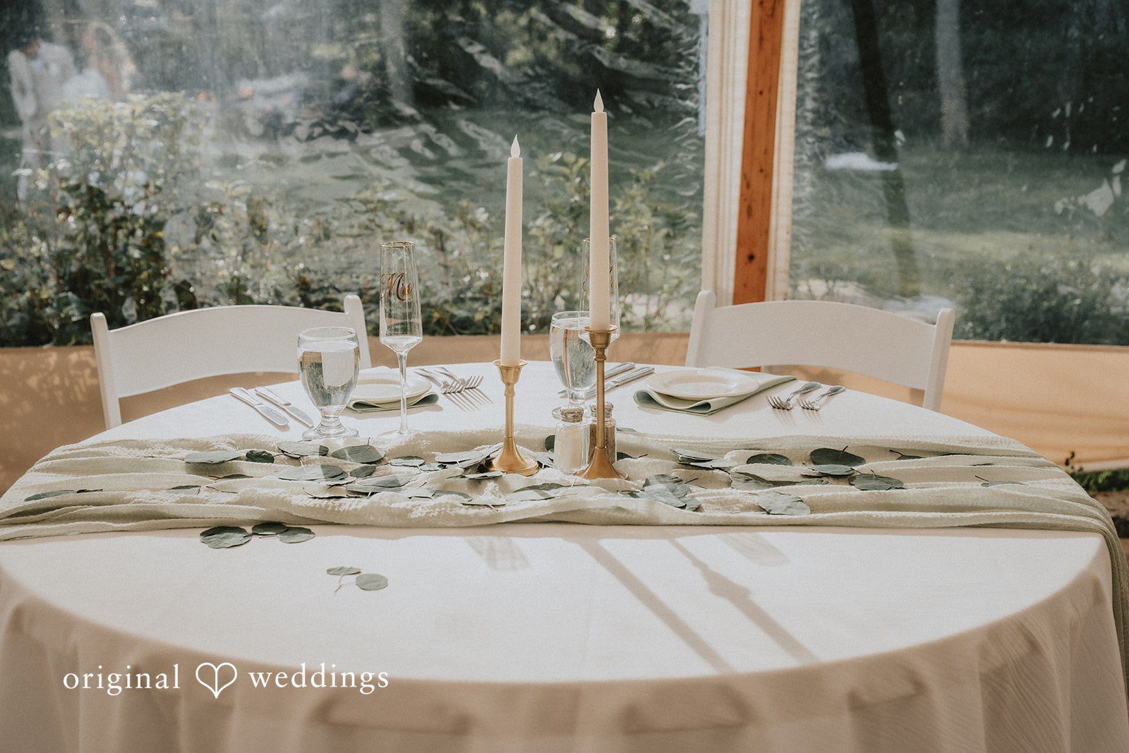 Kaylee + Raul A round wedding reception table with white linens, green runners, and candles.