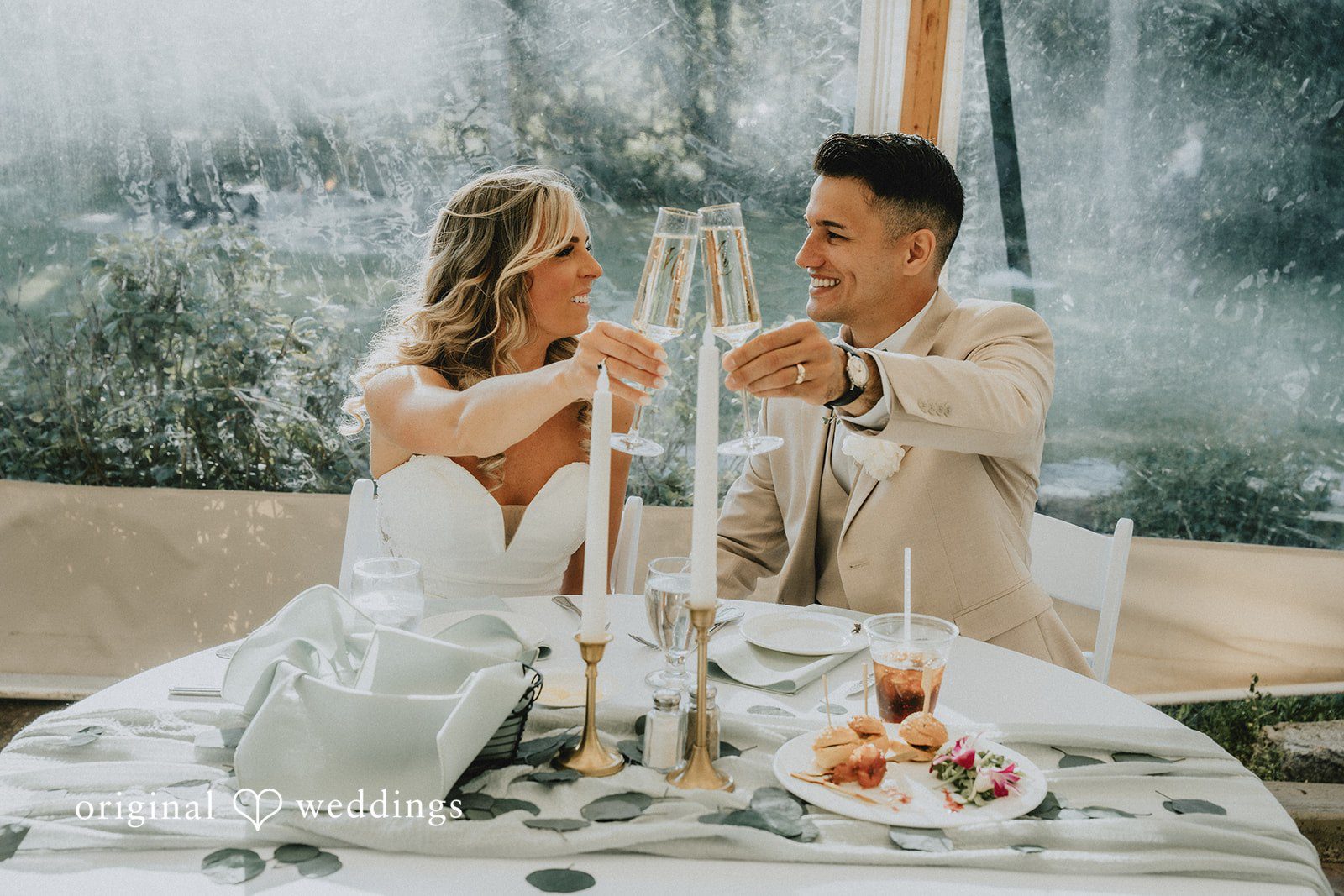 Kaylee + Raul A bride and groom seated at their reception table raising glasses for a toast