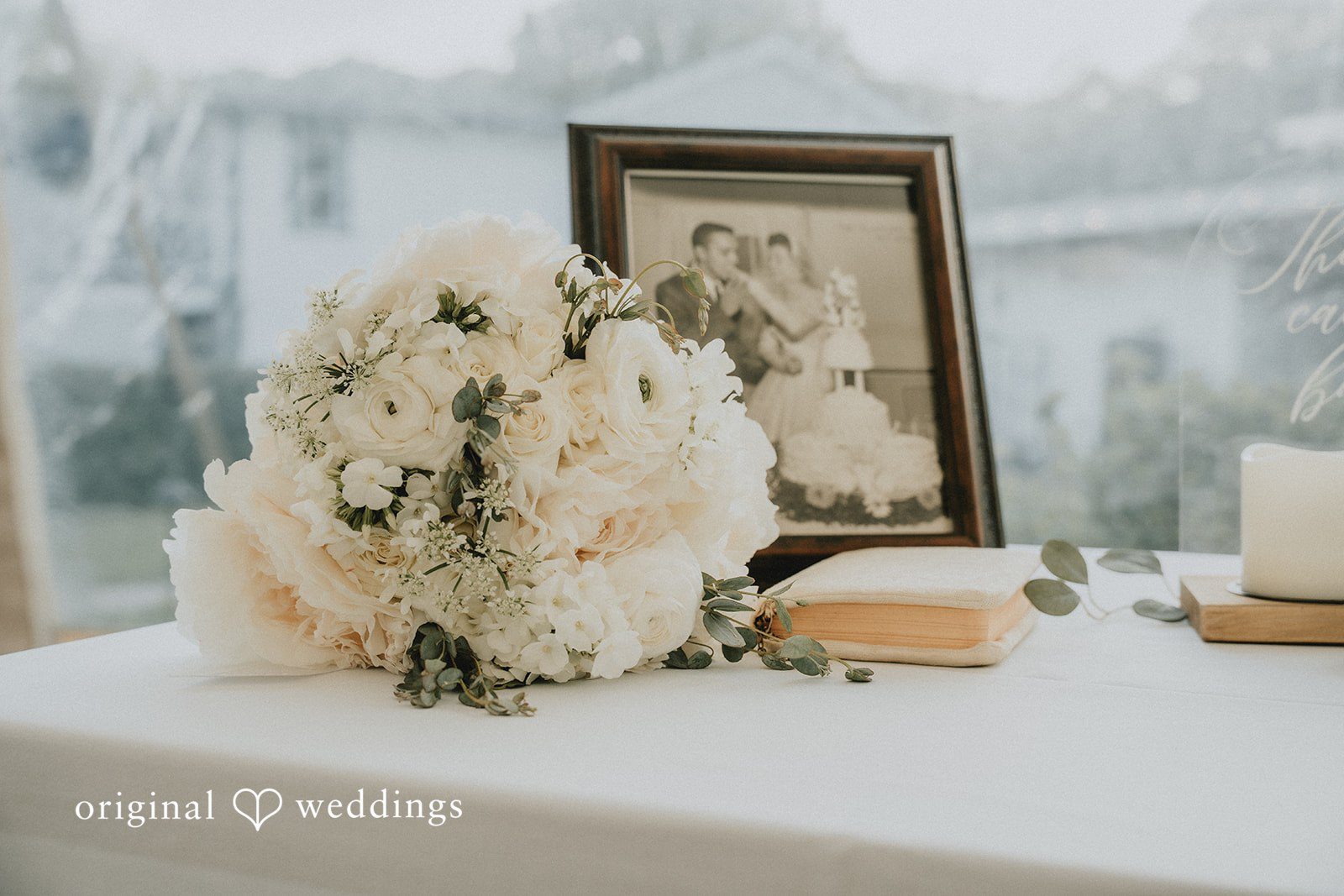 Kaylee + Raul A wedding guest book table featuring a white floral arrangement and framed photos.