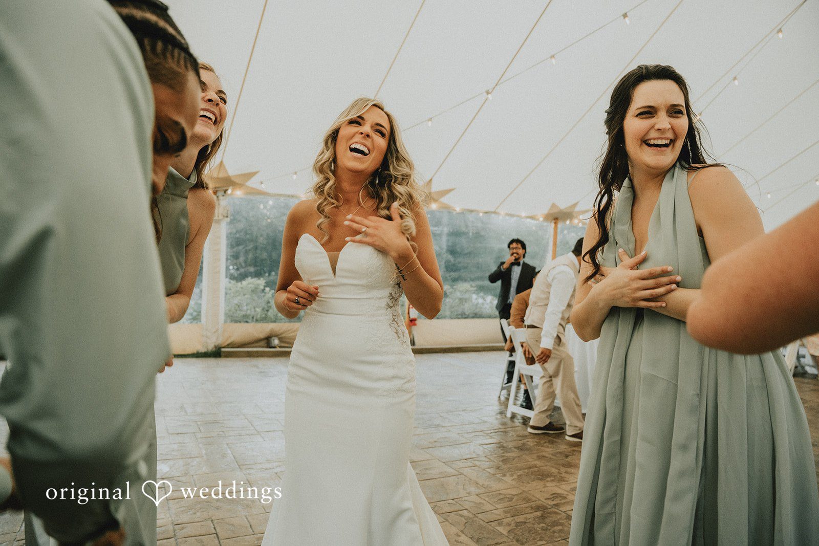 Kaylee + Raul A laughing bride standing alongside a bridesmaid in a sage green dress.
