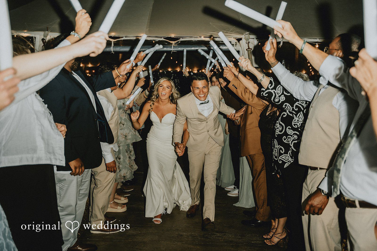 Kaylee + Raul A newlywed couple walking through a cheering crowd of wedding guests holding glow sticks.