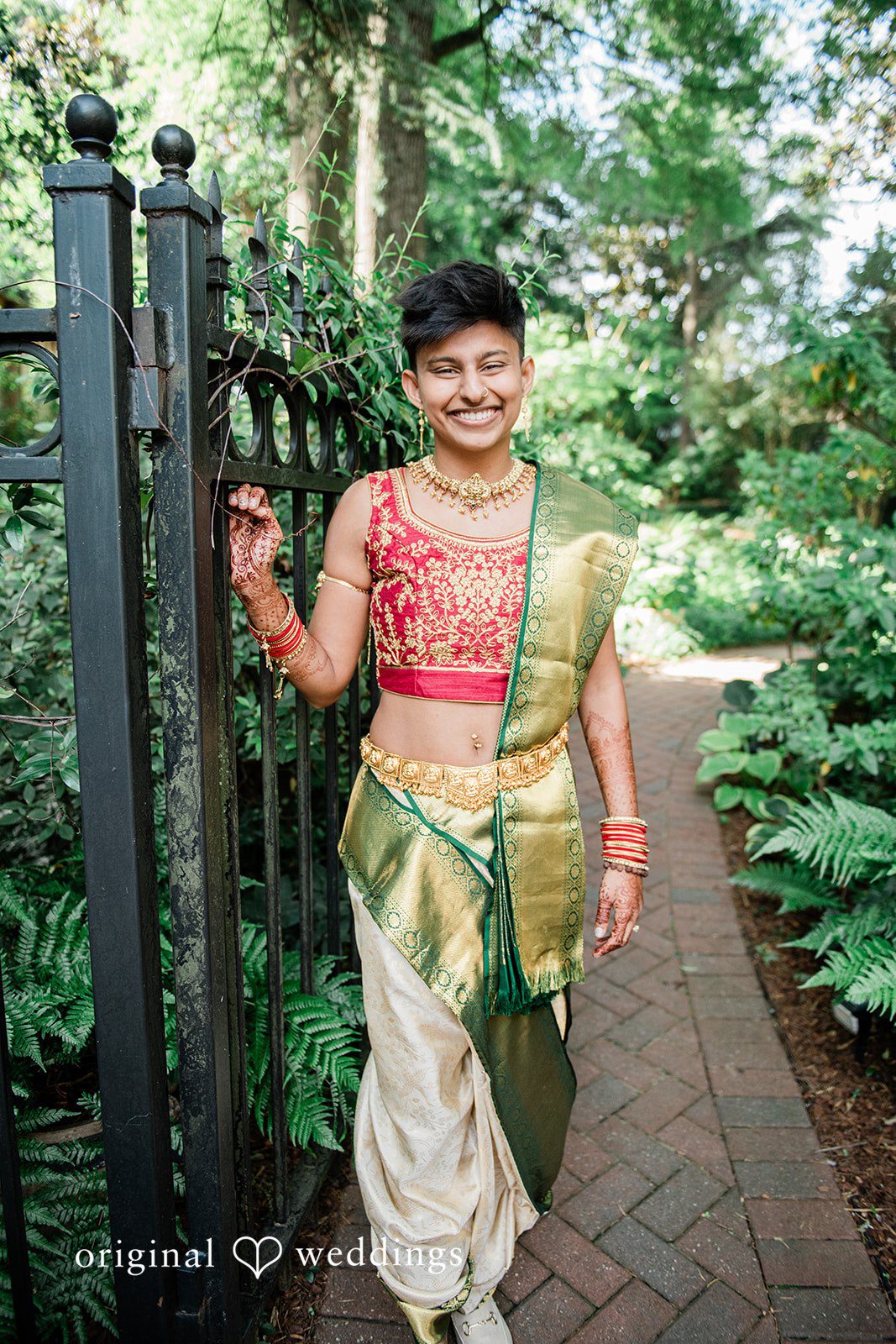 Sonya + Akshaya A smiling groom in traditional attire standing by an ornate black gate.