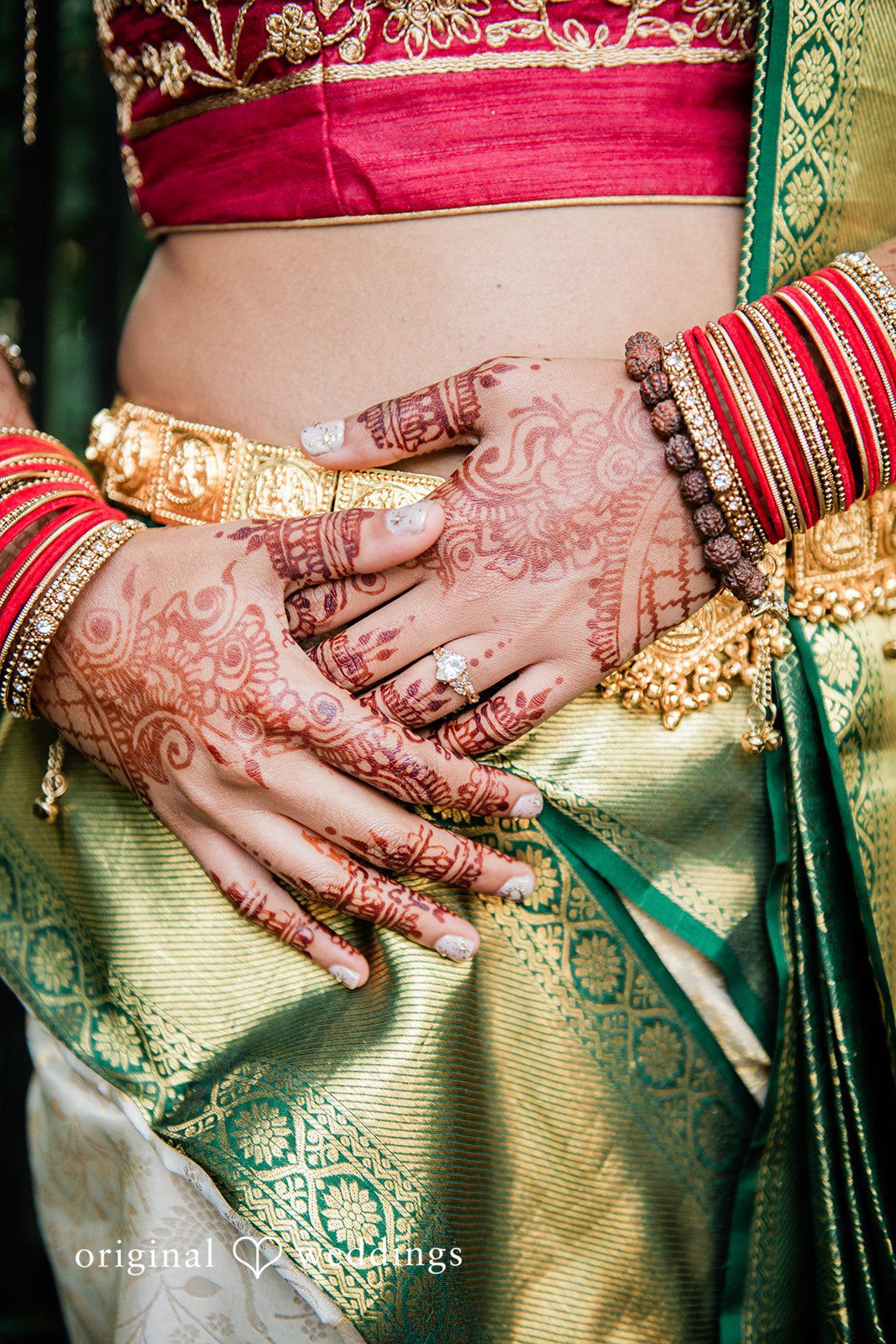 Sonya + Akshaya Close-up of a bride's henna-decorated hands resting on her green saree.